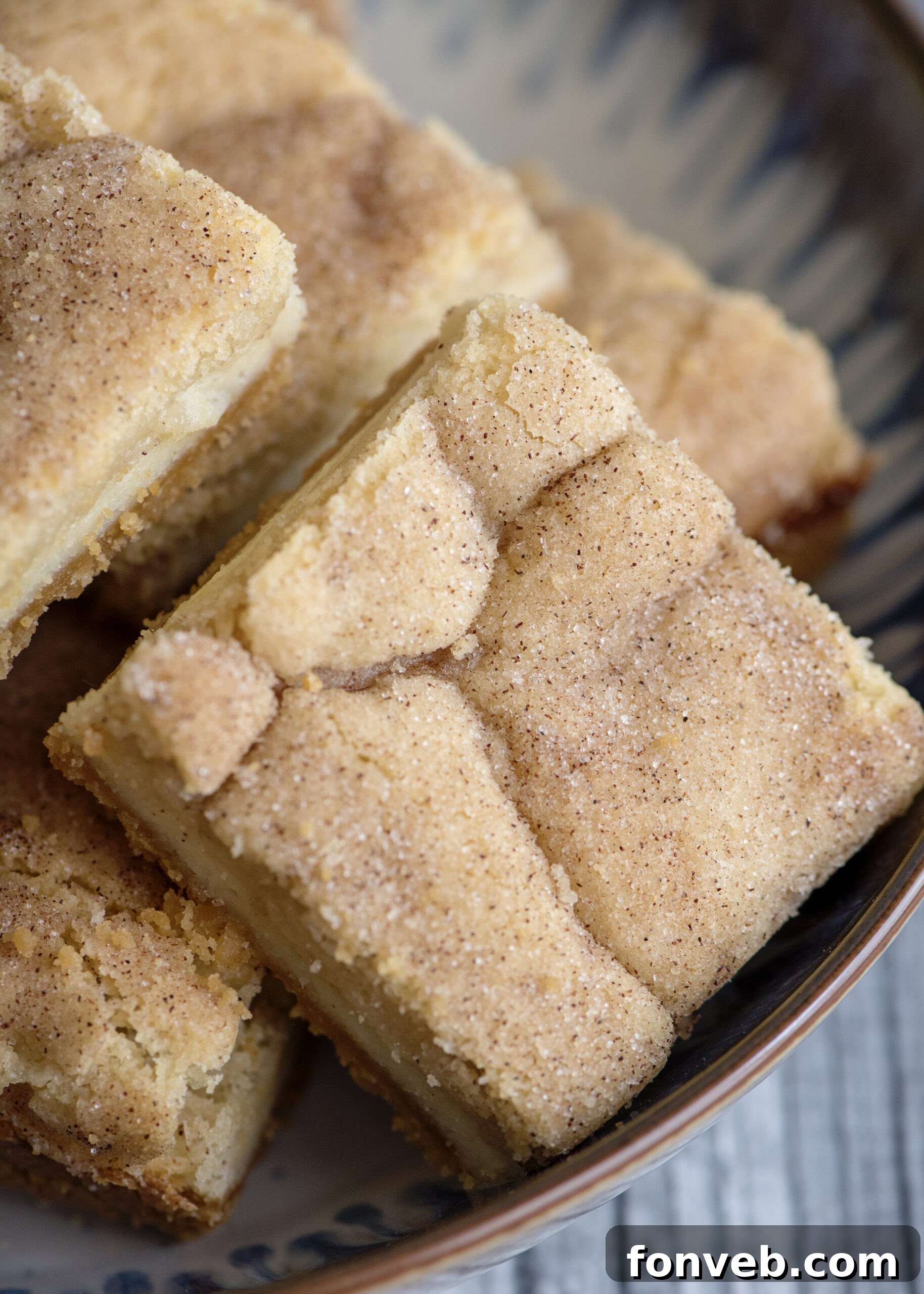 A hand reaching for a piece of Snickerdoodle Cheesecake Bar on a white plate