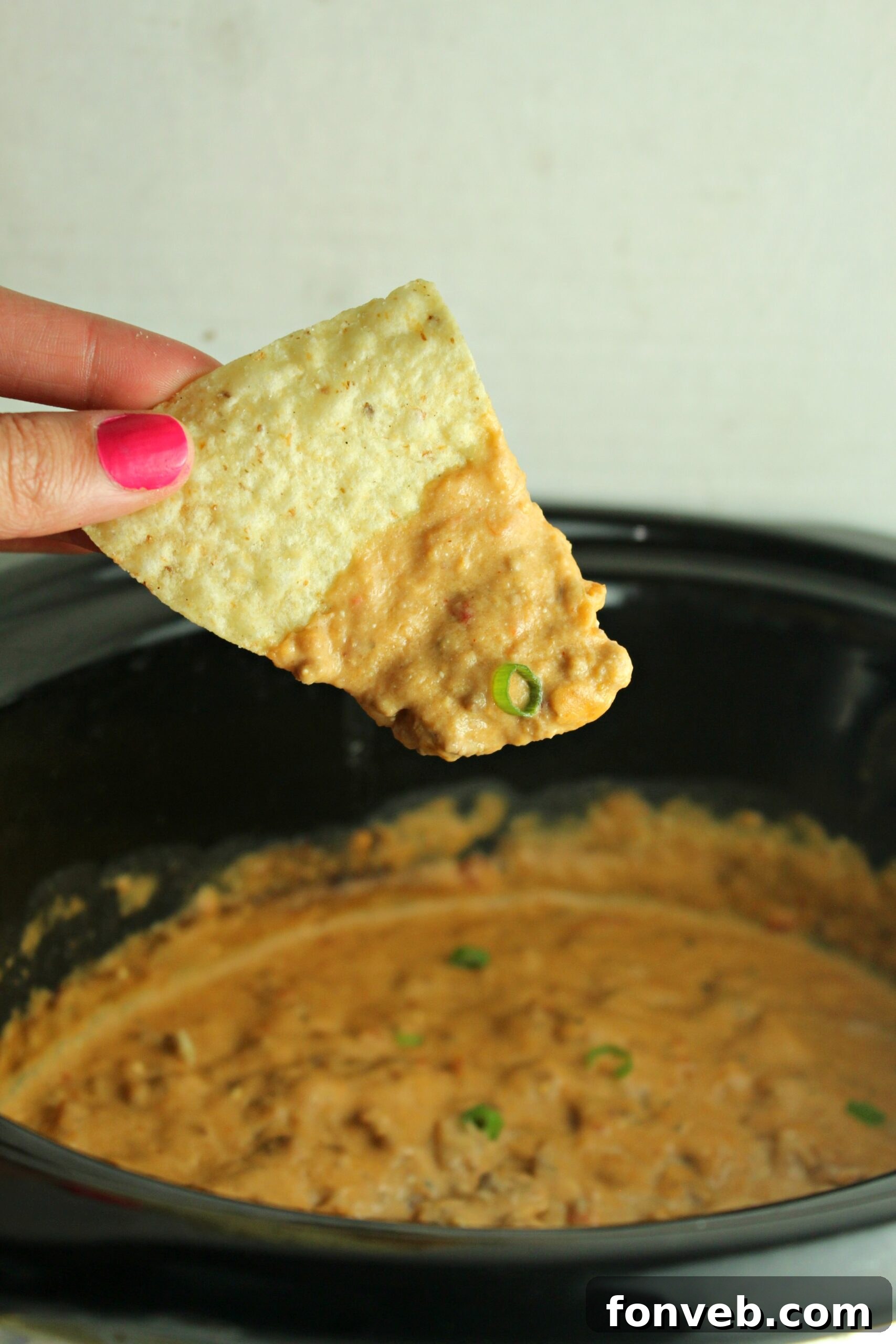 Serving spoons dipping into a large pot of warm taco dip