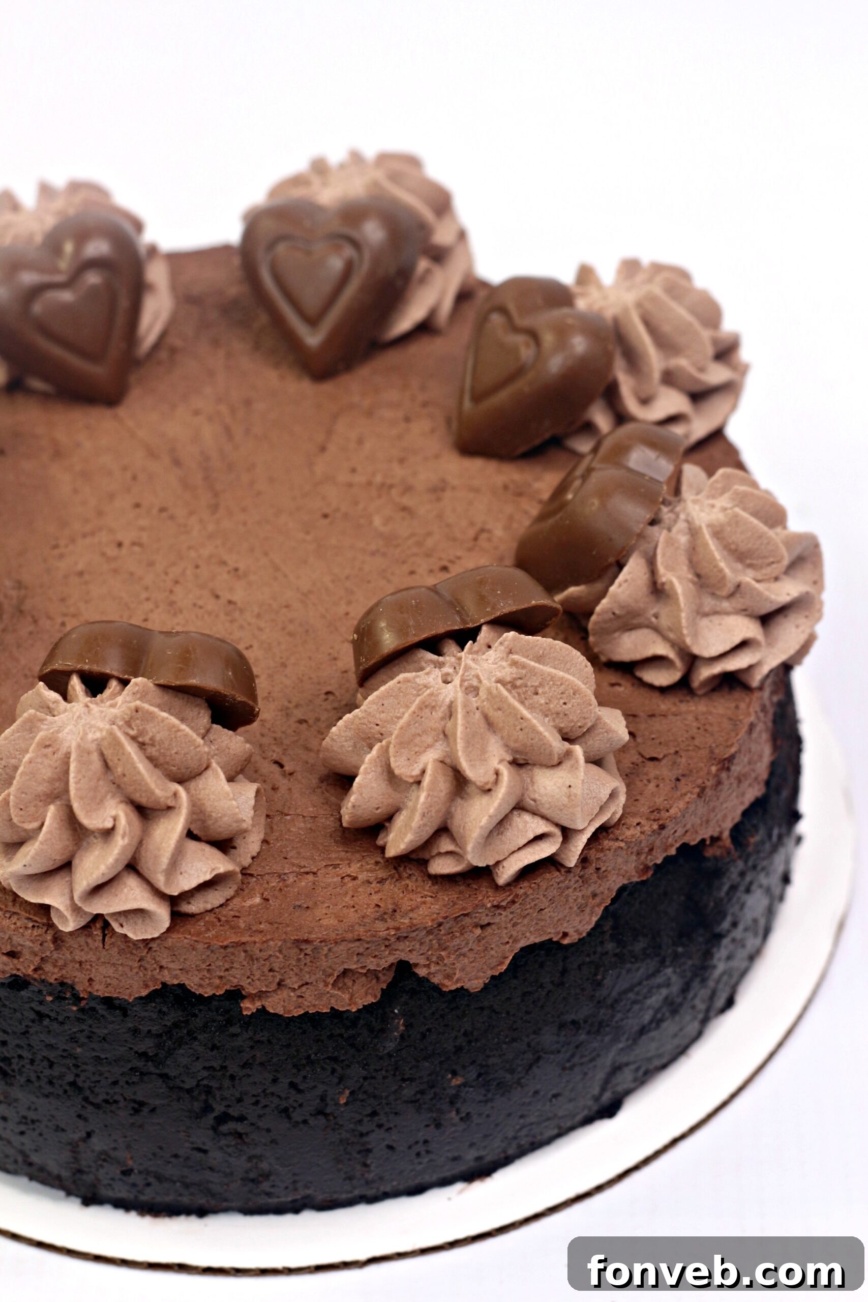 A slice of Triple Chocolate Layered Godiva Cheesecake served on a plate, adorned with chocolate hearts and a sprinkle of chocolate shavings.