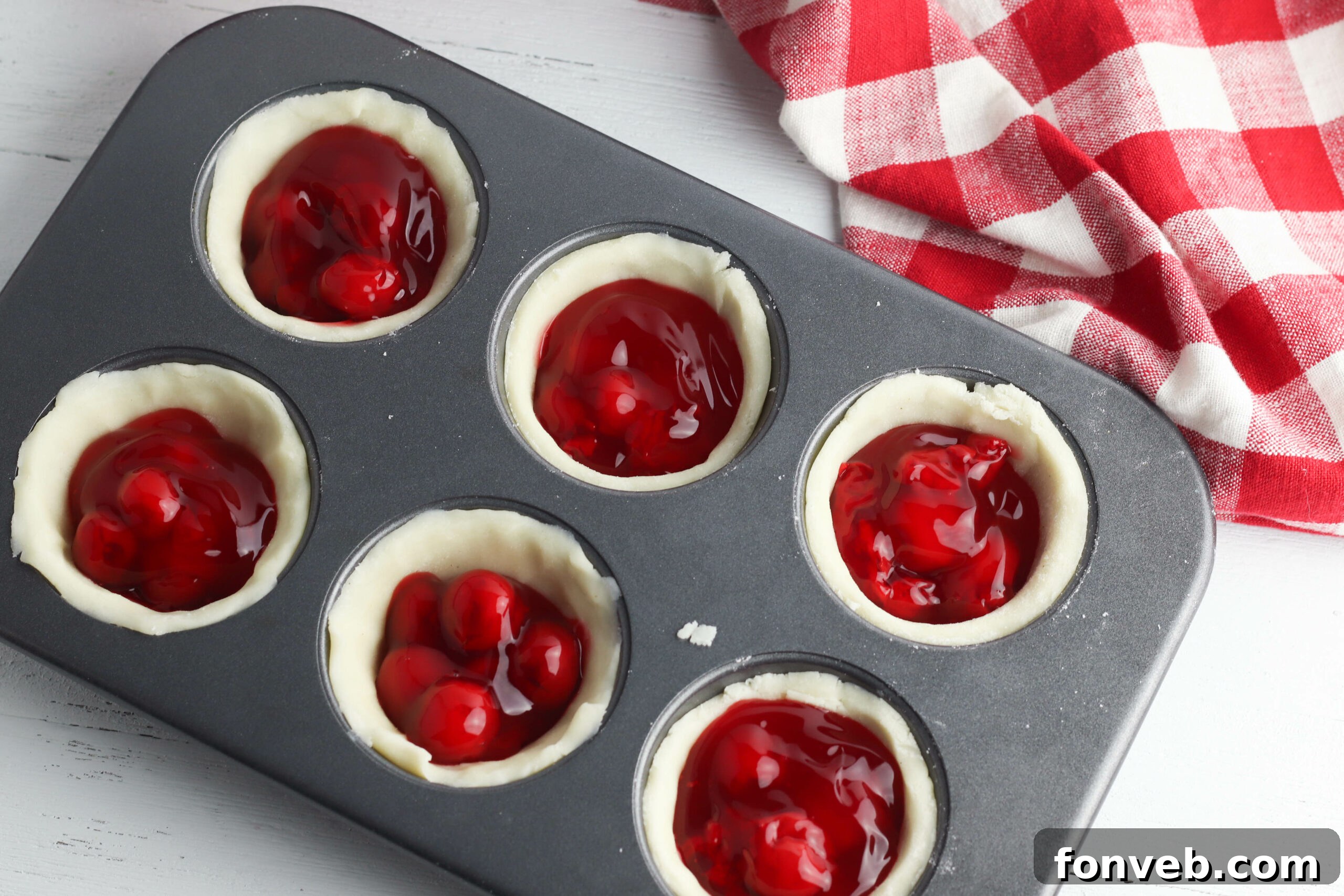 A selection of baked mini cherry pies, some with lattice tops and others with full crusts, arranged on a cooling rack.
