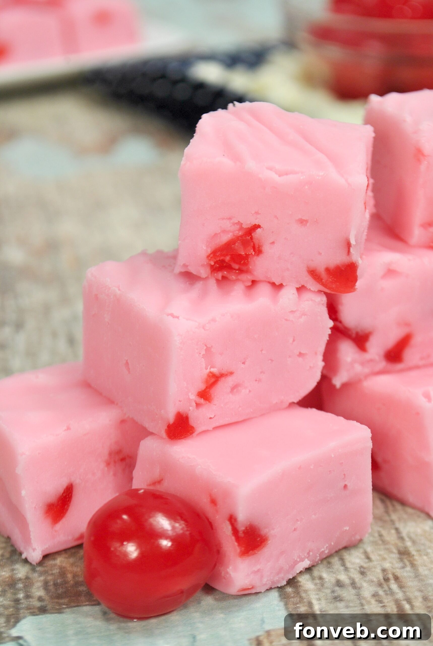 A close-up of a hand holding a piece of cherry fudge, revealing its moist texture and cherry chunks.