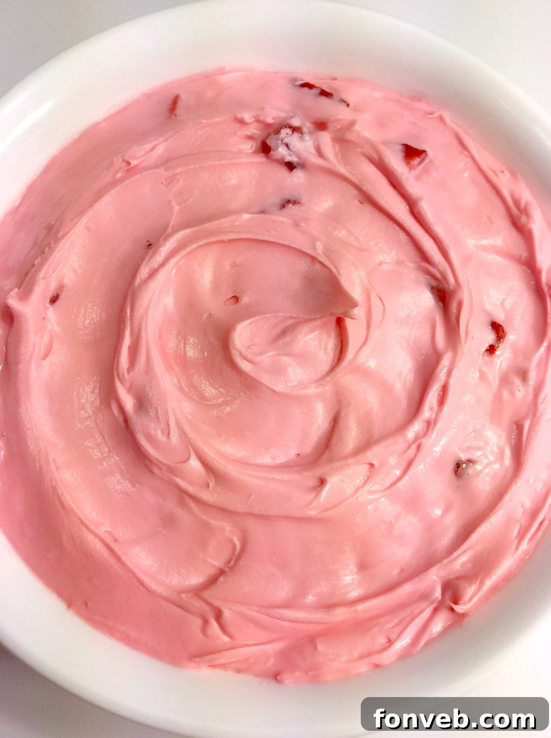 Freshly piped strawberry buttercream frosting on a cupcake, garnished with a whole strawberry.