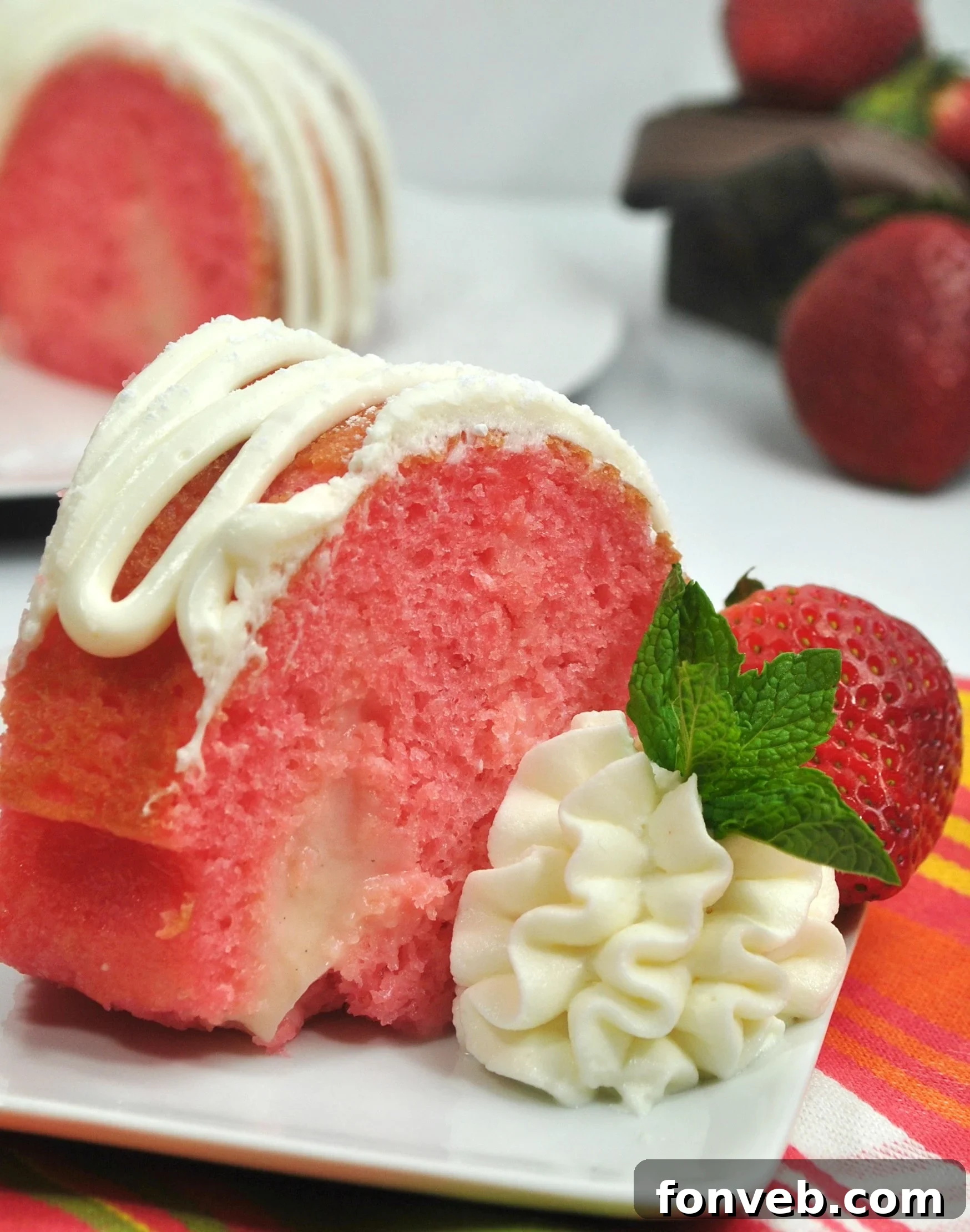 A beautifully sliced Strawberries & Cream Bundt Cake with generous cream cheese frosting, revealing fresh strawberry pieces inside.