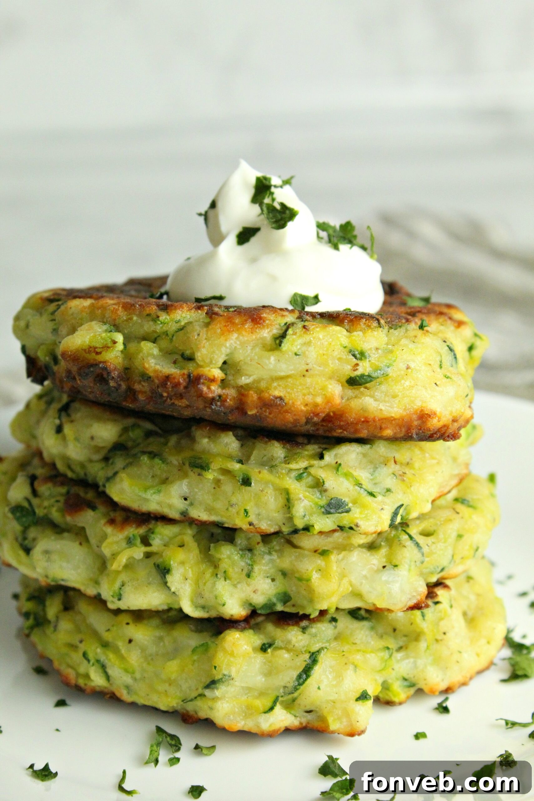 Close-up of a stack of cheesy zucchini pancakes with melted cheese visible