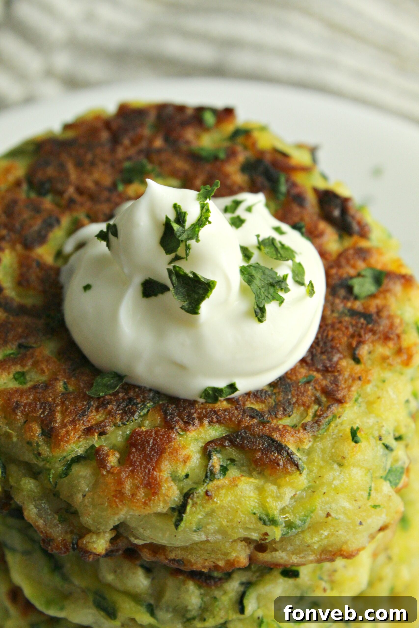 A hand holding a cheesy zucchini pancake, showing its golden texture