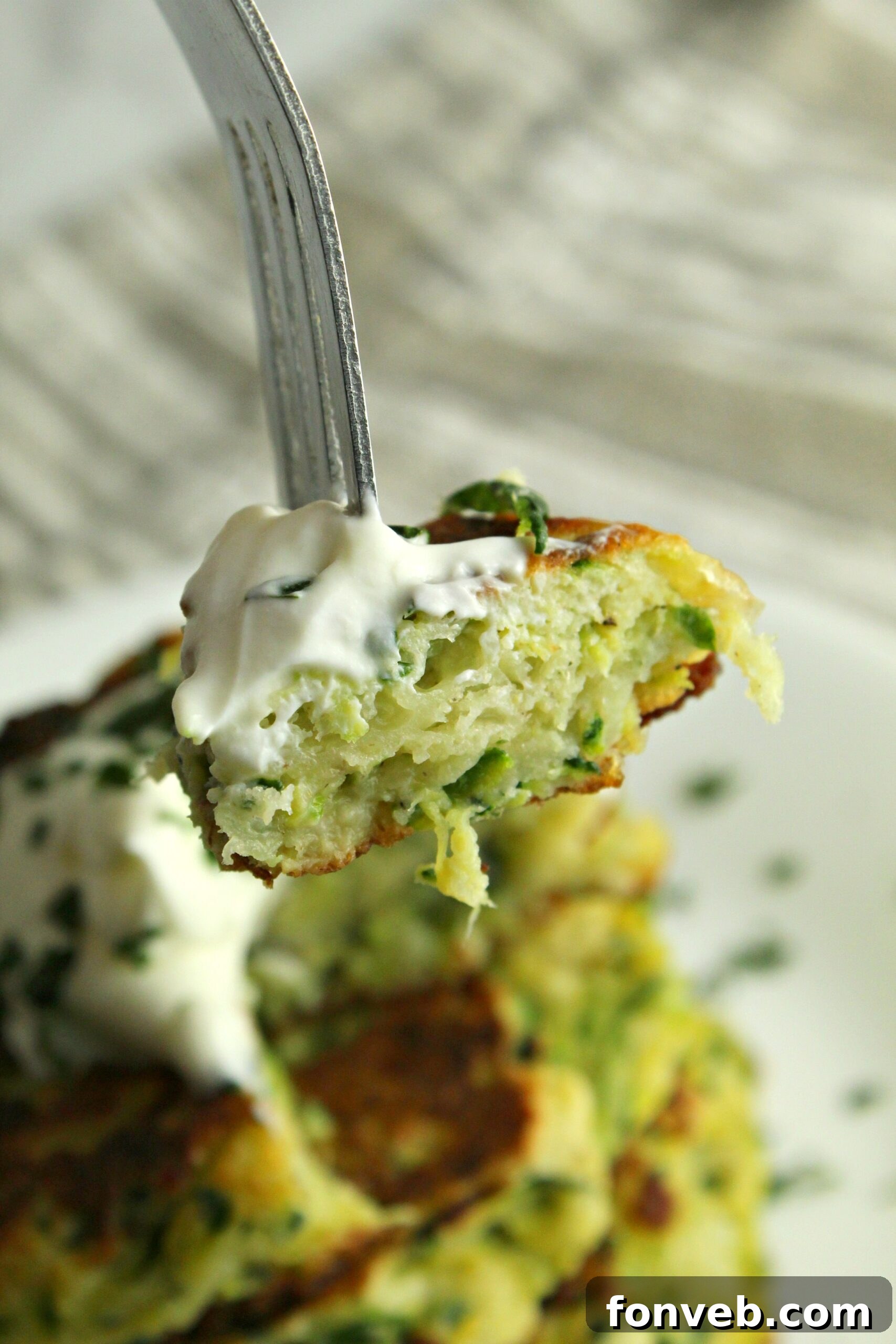 A serving of cheesy zucchini pancakes with a spoonful of sour cream and fresh dill
