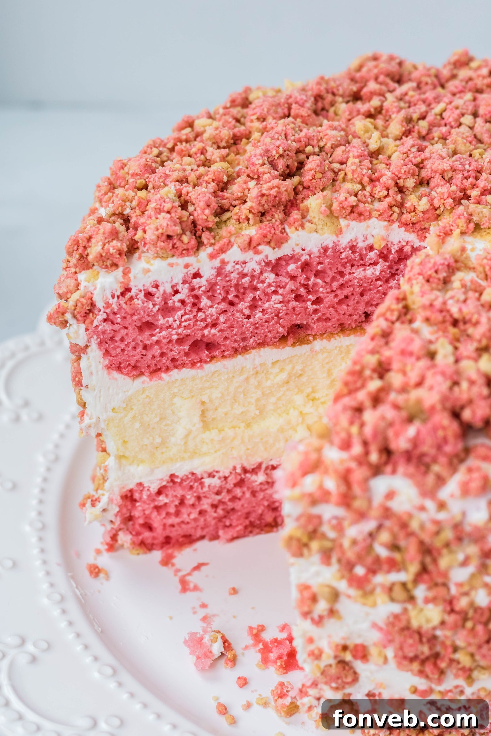 Ultimate Strawberry Shortcake Cheesecake 3 A beautifully decorated Strawberry Shortcake Cheesecake Cake on a white cake stand, with one slice removed, revealing the intricate layers of cake, cheesecake, and frosting.