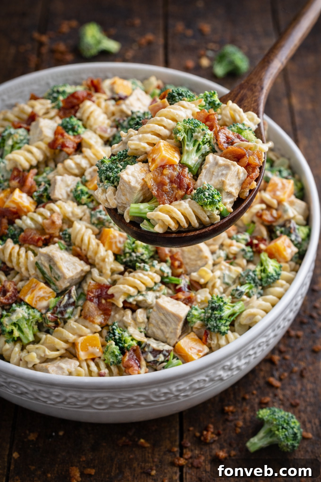 Chicken Bacon Broccoli Pasta Salad in a big pretty white designed bowl with a bamboo spoon lifting up a bite