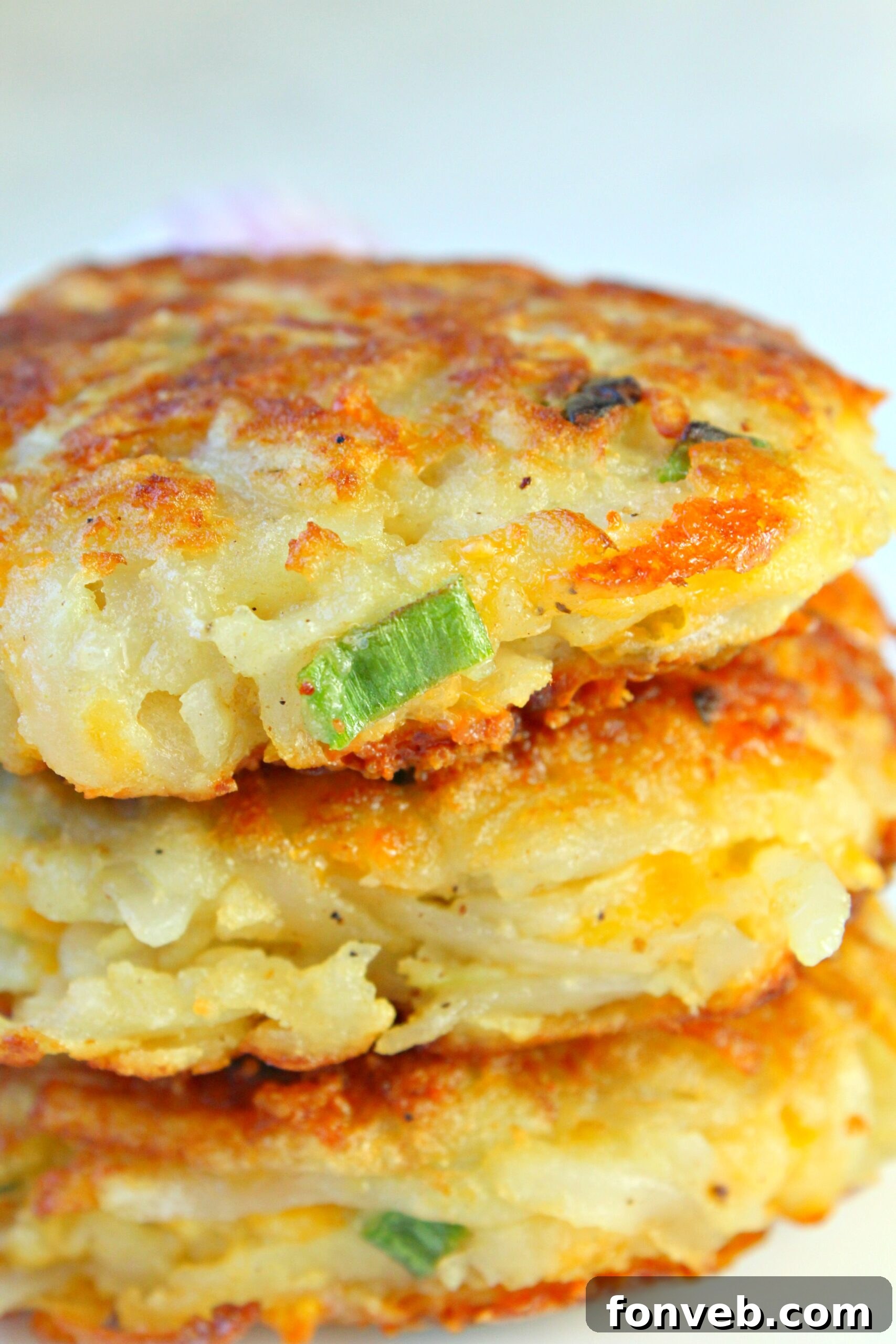 A close-up of a stack of golden hash brown patties, showing the melted cheese inside.