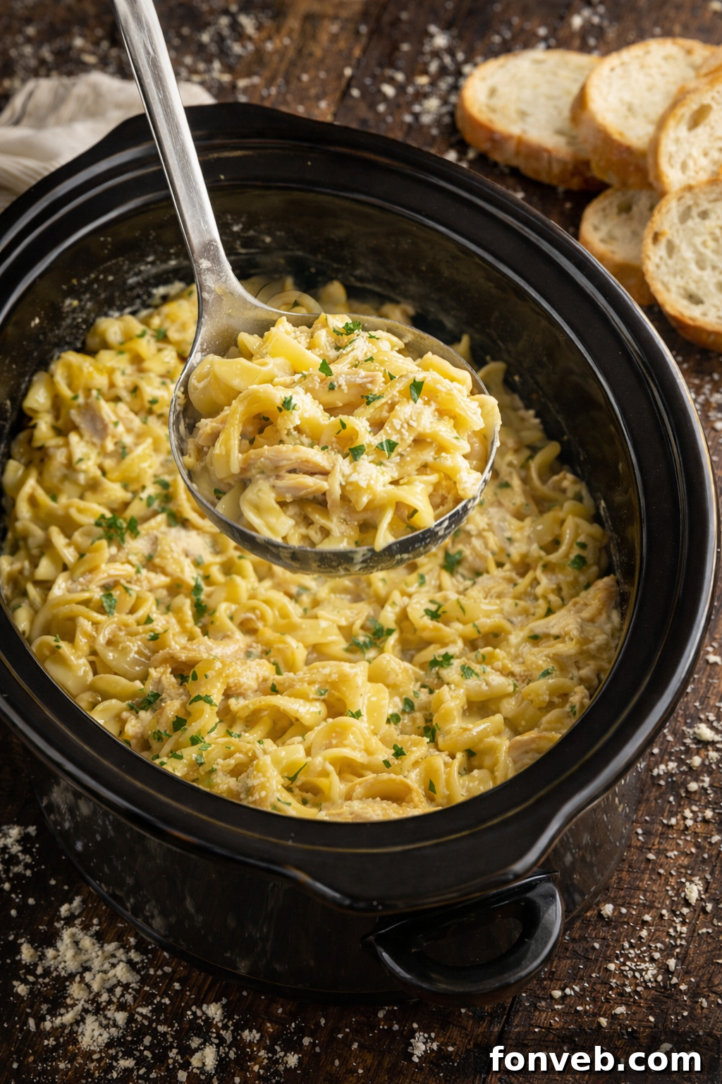 A large serving spoon lifting a portion of Slow Cooker Chicken and Noodles from the slow cooker, showing its rich texture.