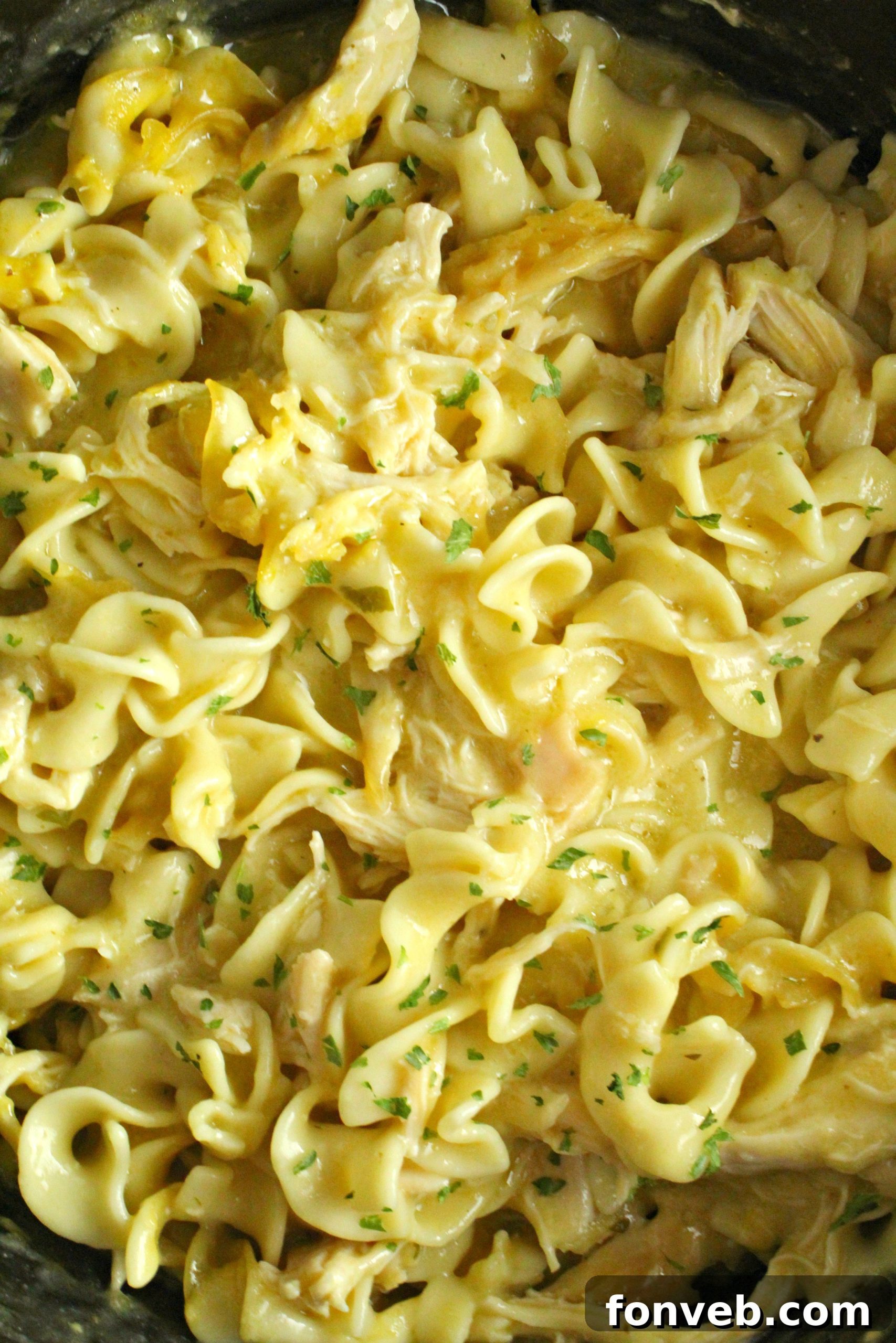A spoonful of Slow Cooker Chicken and Noodles being lifted from the slow cooker, showing the thick sauce and tender ingredients.