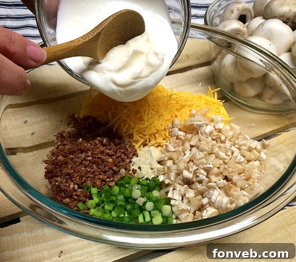 The savory filling ingredients for stuffed mushrooms, including shredded cheese, crumbled bacon, and creamy bases, mixed in a bowl.