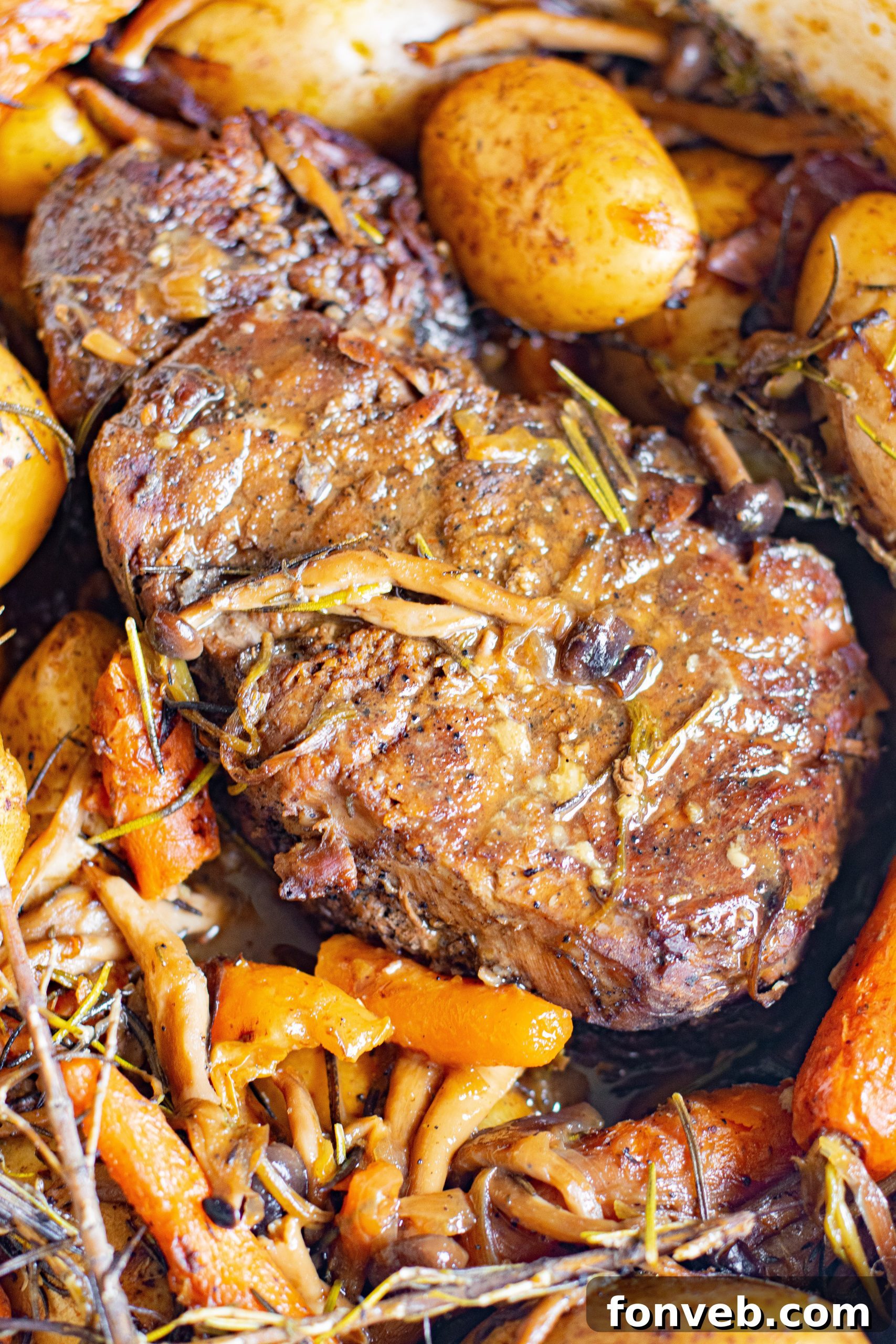 A vibrant display of whole pot roast surrounded by cooked baby potatoes, carrots, and mushrooms.