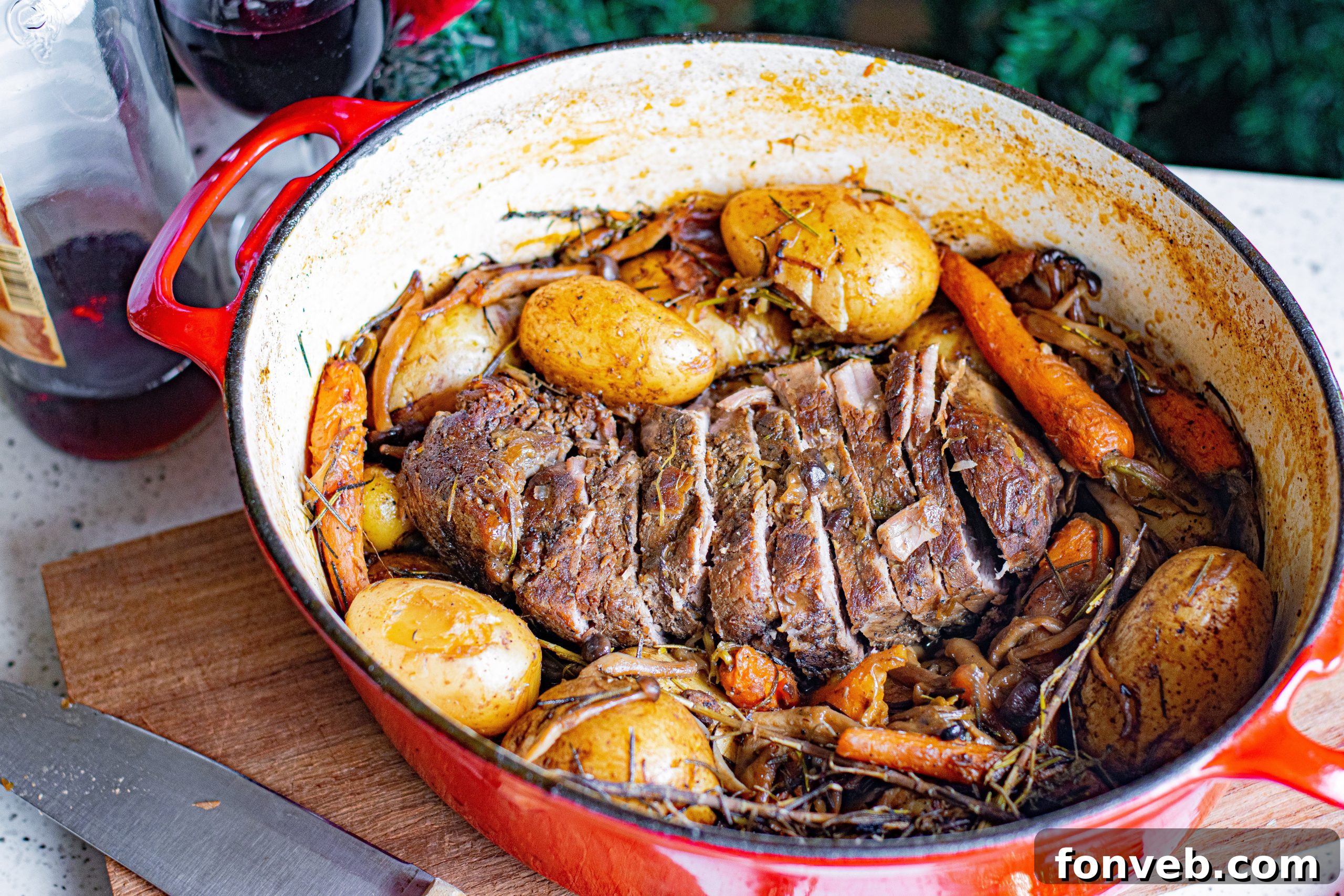 A bottle of red wine and glasses set on a table, with a blurred pot roast in the background.