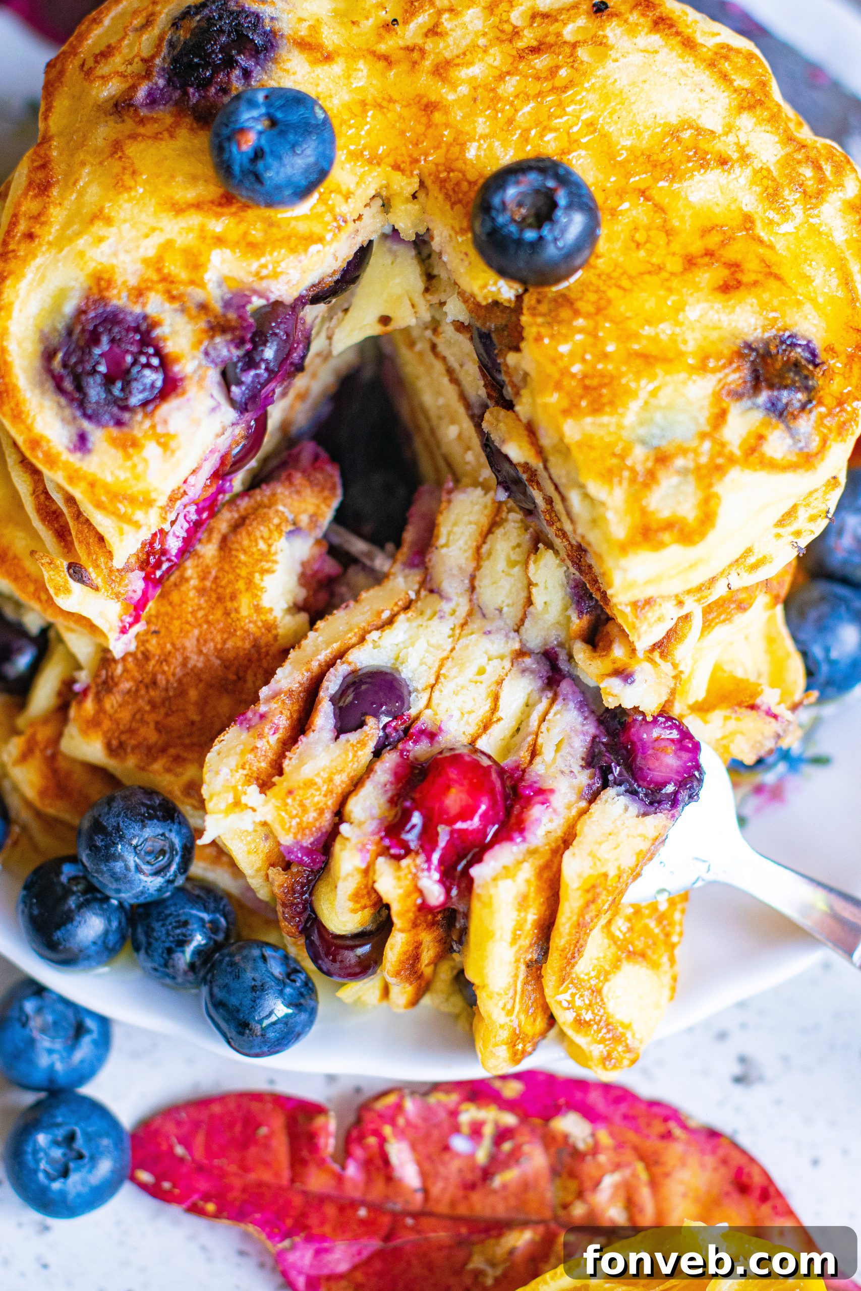 A tantalizing close-up shot of a stack of blueberry cream cheese pancakes, adorned with a melting pat of butter and rich maple syrup, emphasizing their moist texture.