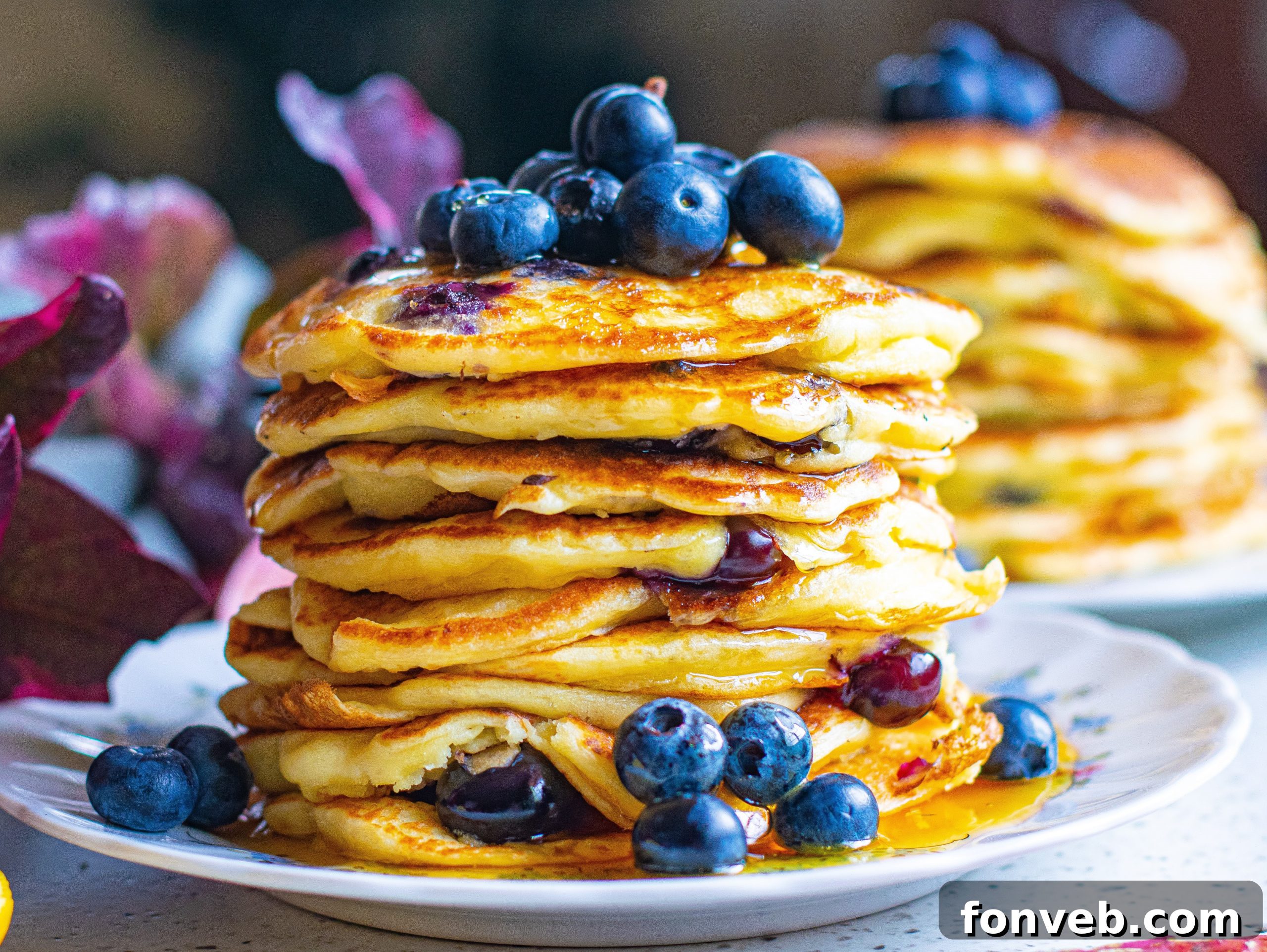 An aesthetically pleasing large stack of fluffy blueberry cream cheese pancakes, artfully arranged with fresh blueberries and a generous pour of maple syrup.