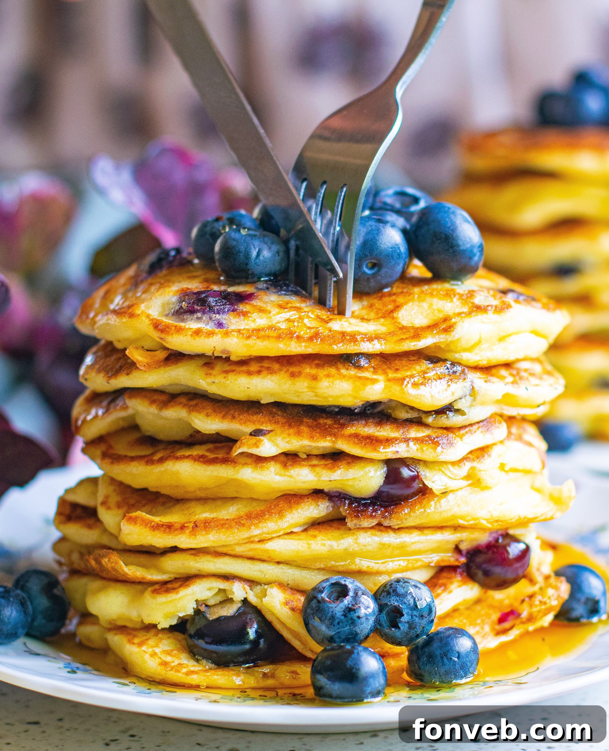 A serving of blueberry cream cheese pancakes on a white plate, artfully garnished with fresh blueberries and a drizzle of syrup, ready to be enjoyed.