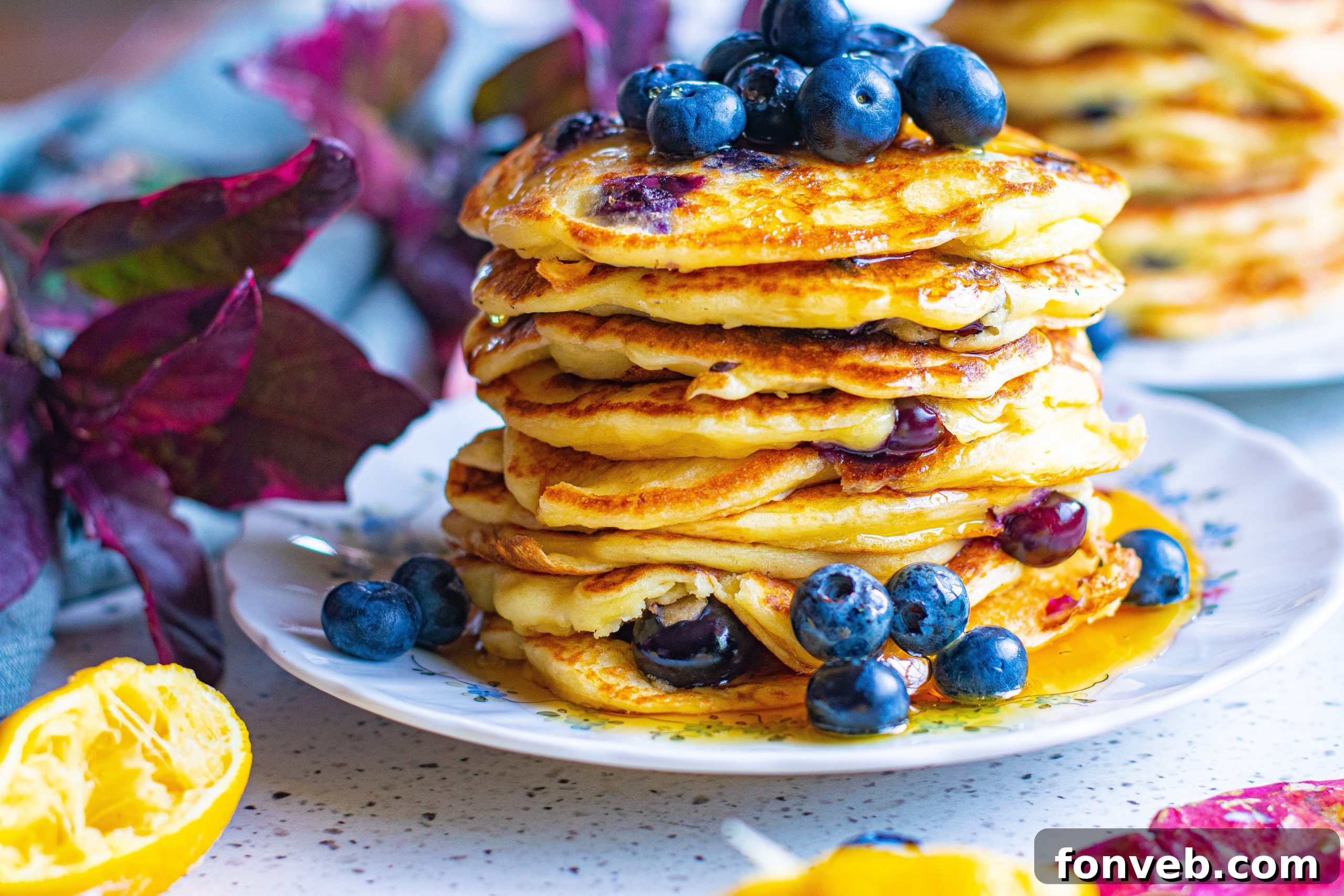 Close-up of a stack of blueberry cream cheese pancakes with melting butter and thick, flowing maple syrup.