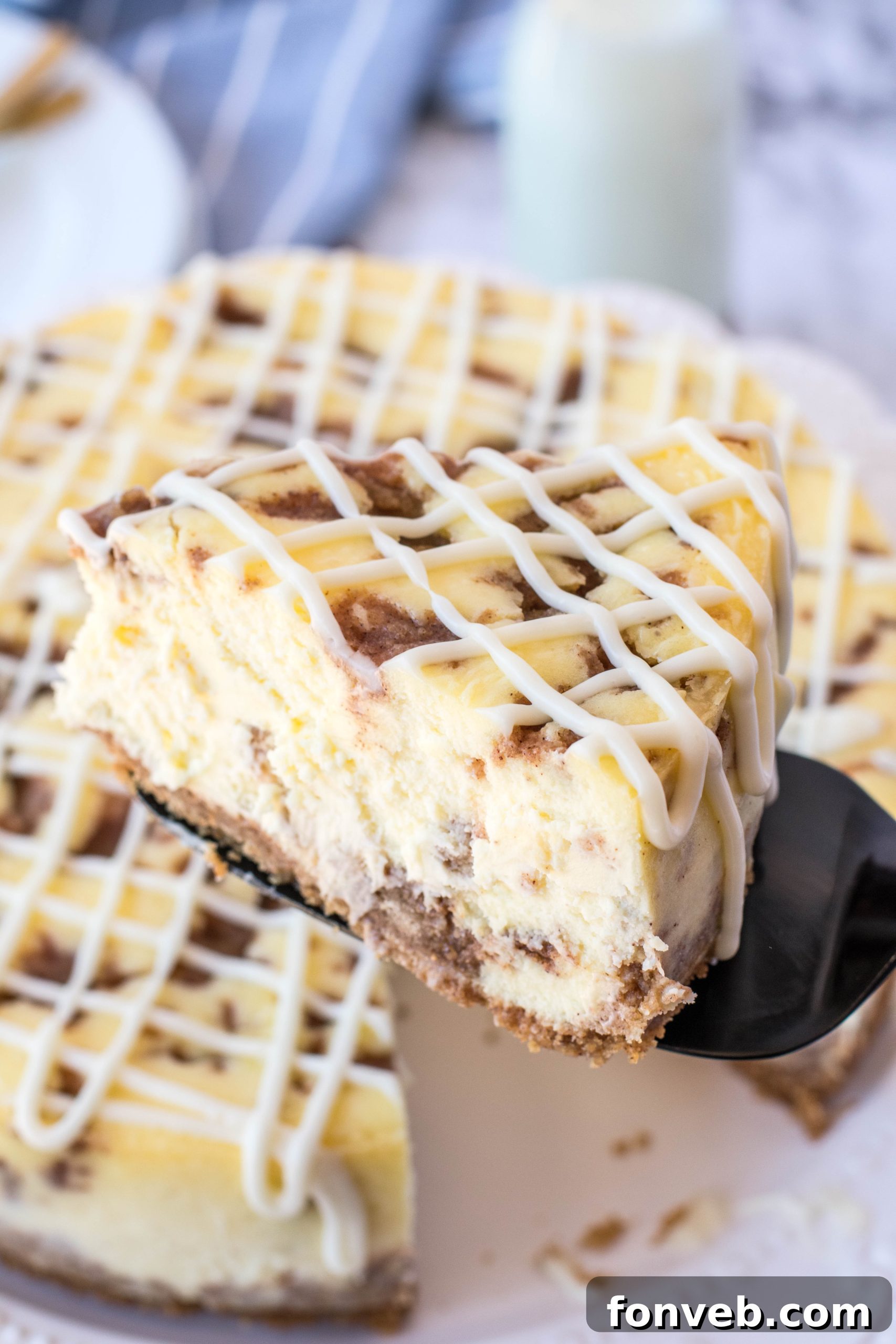 A slice of Cinnamon Roll Cheesecake with a visible cinnamon swirl pattern, drizzled generously with cream cheese frosting.