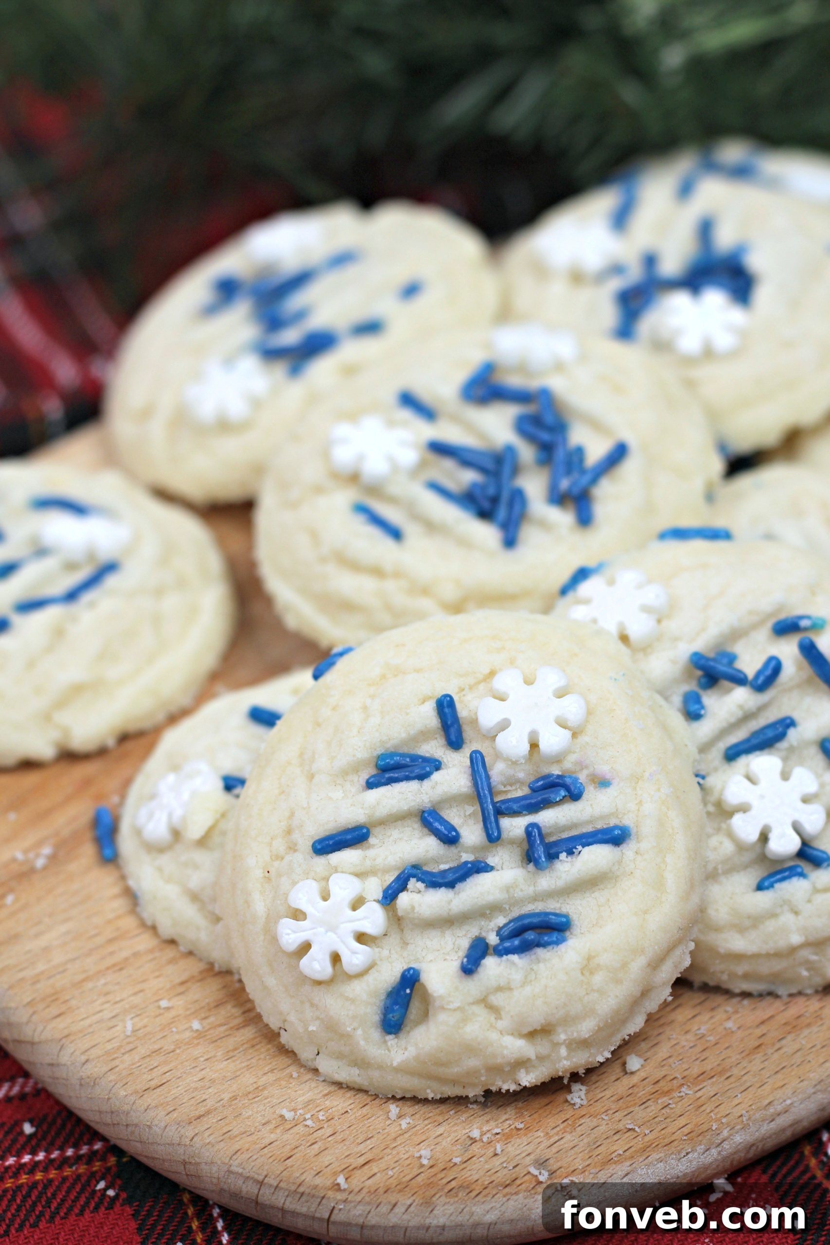 A close-up of a single whipped shortbread cookie with blue and white snowflake sprinkles, showing its delicate texture.