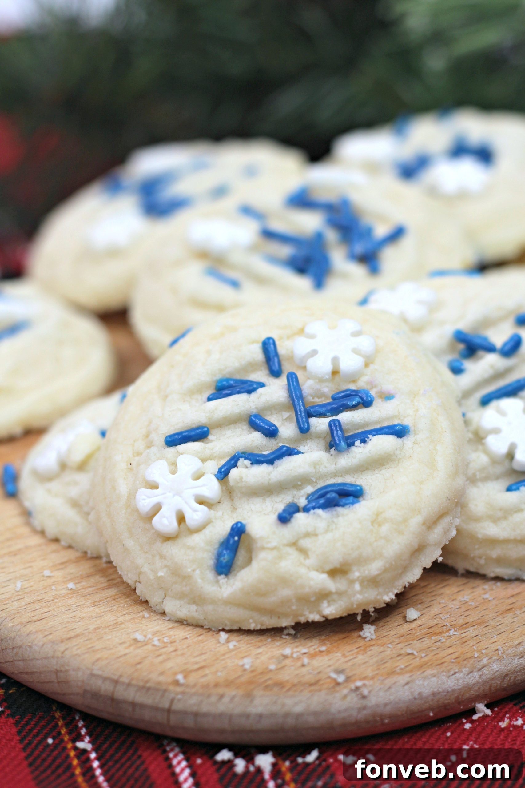 A close-up view of two round whipped shortbread cookies, one decorated with blue sprinkles, resting on a white surface.