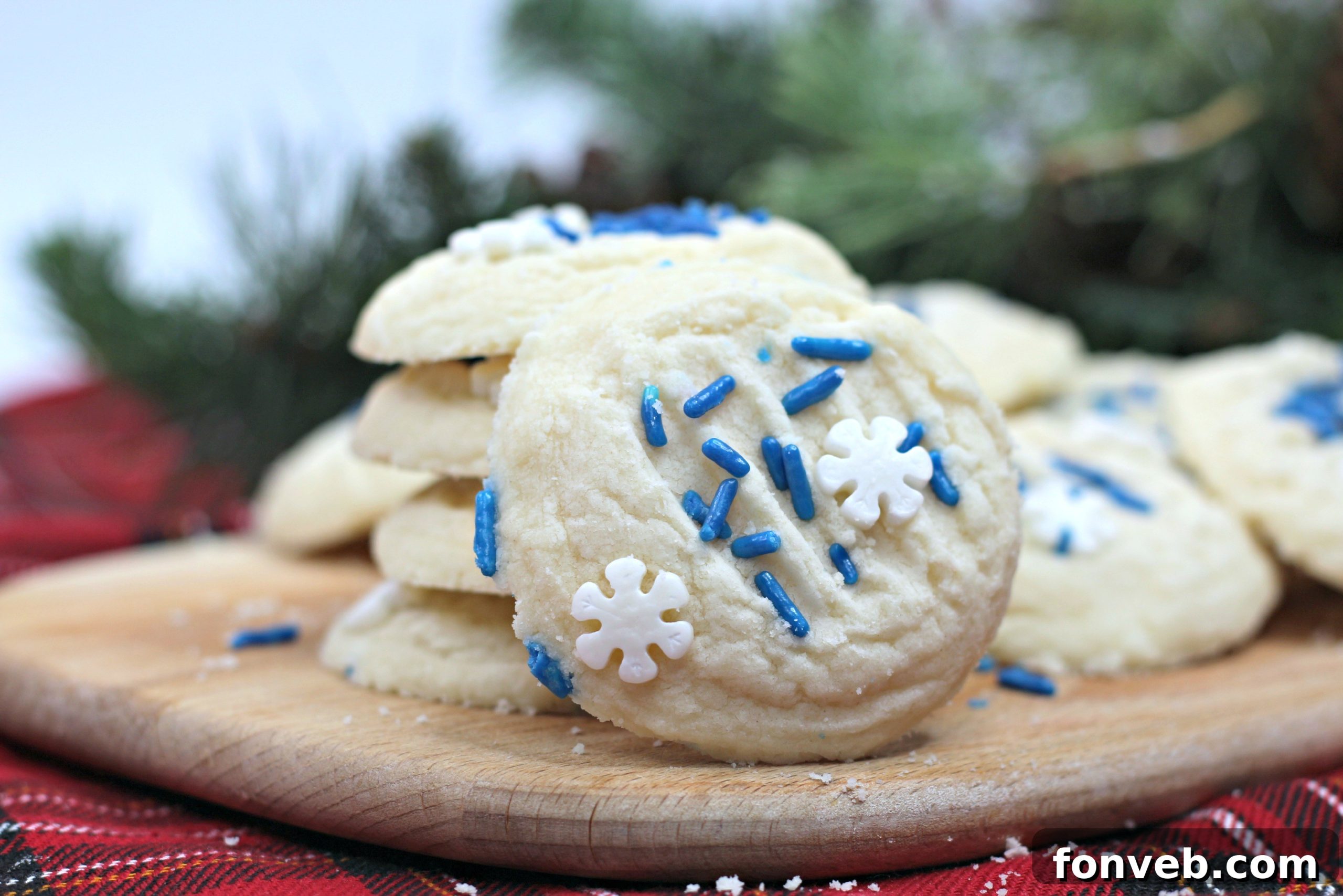 Two hands gently holding a small whipped shortbread cookie decorated with blue and white sprinkles.