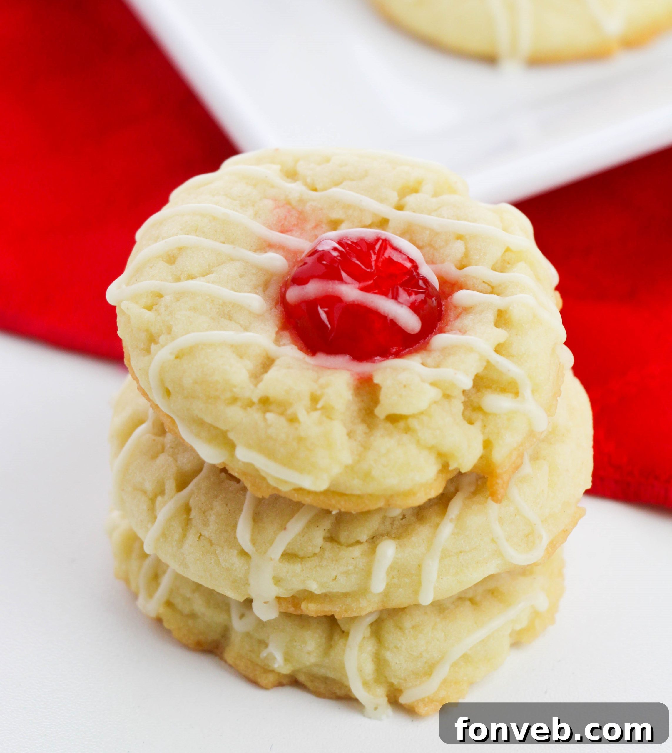 Eggnog Thumbprint Cookies with bright red cherry centers and an icing drizzle on a white plate