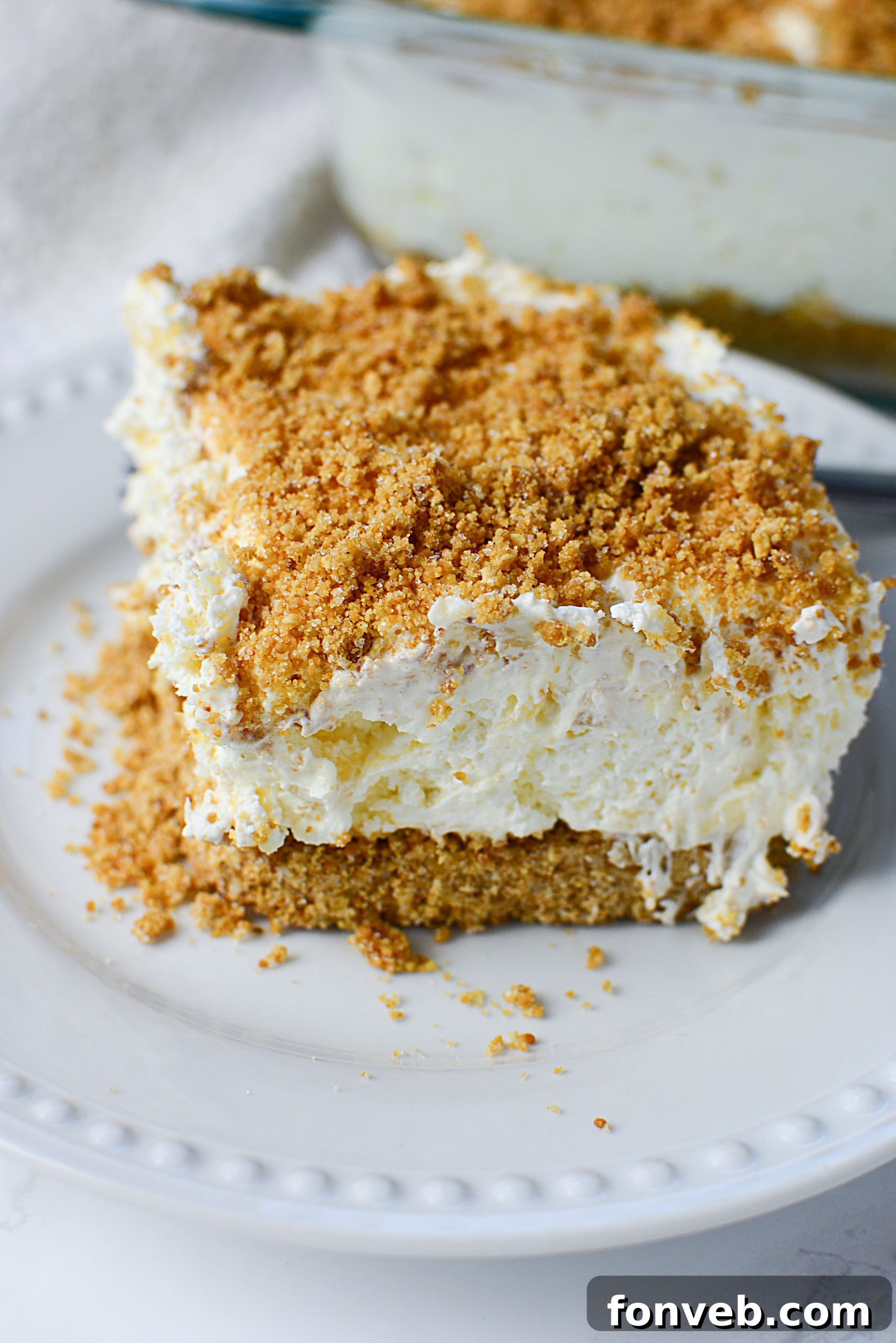 A vibrant, refreshing slice of pineapple cream dessert, garnished with fresh pineapple wedges and mint, showcasing its creamy texture and crumbly crust.