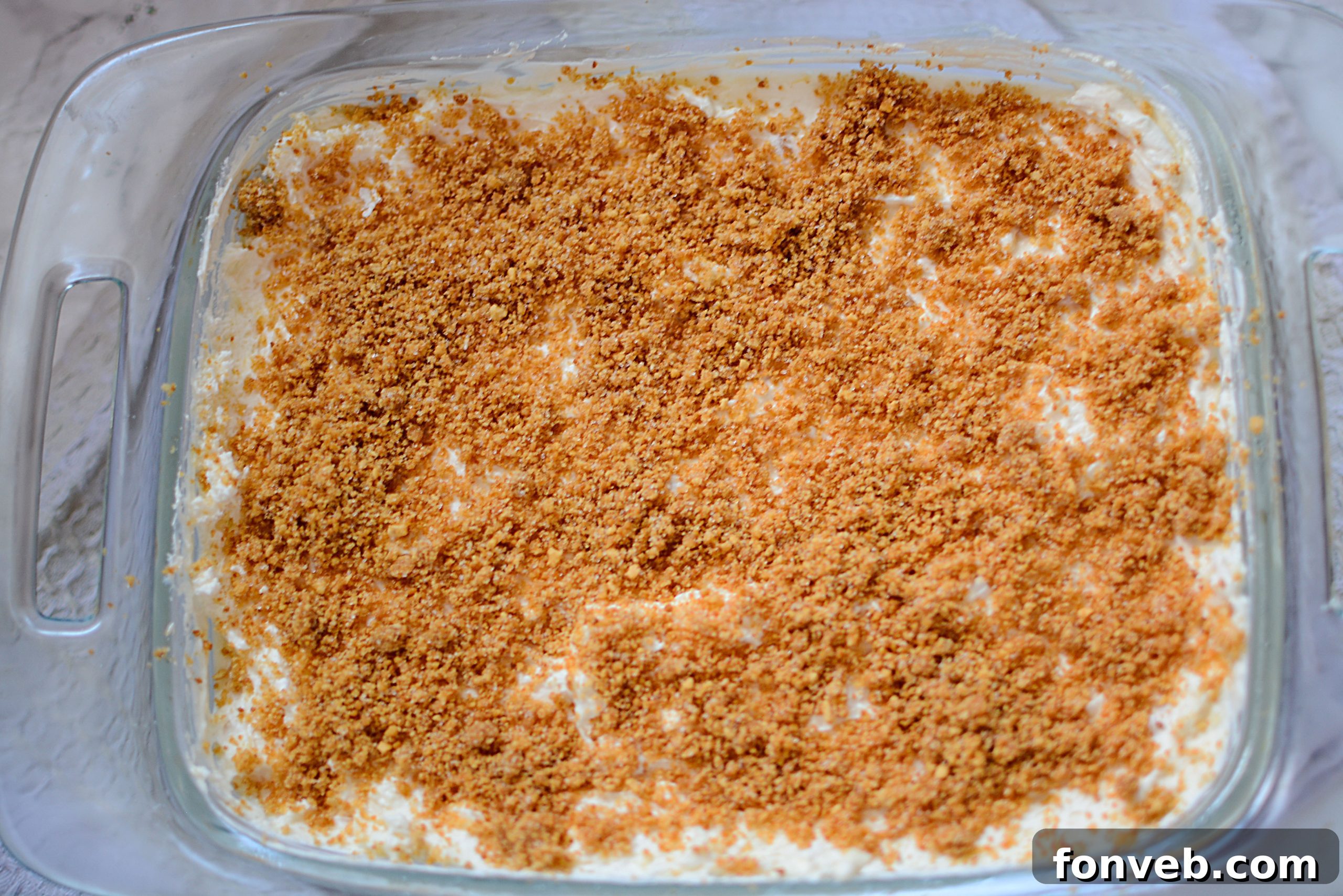 Close-up of a generously sized pan of no-bake pineapple cream dessert, ready to be sliced, highlighting its smooth, pale yellow filling and golden-brown crumb topping.