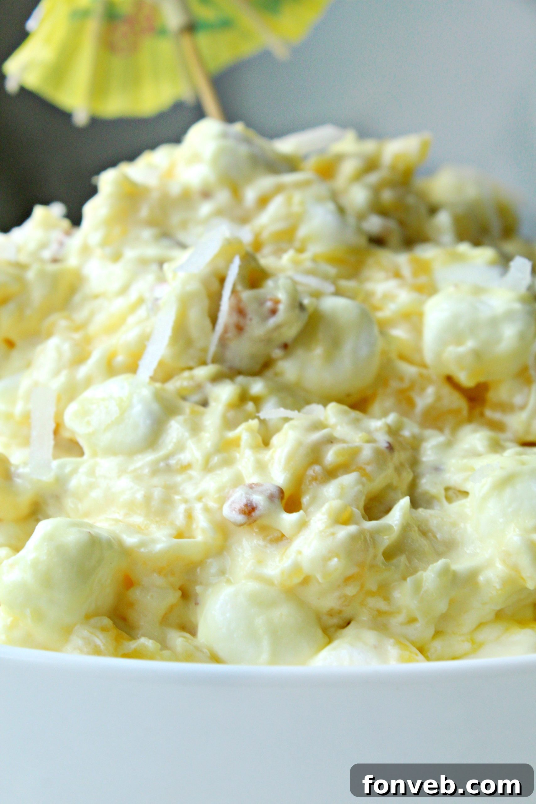 A large serving of Piña Colada Fluff in a white bowl with a spoon, garnished with a cherry.