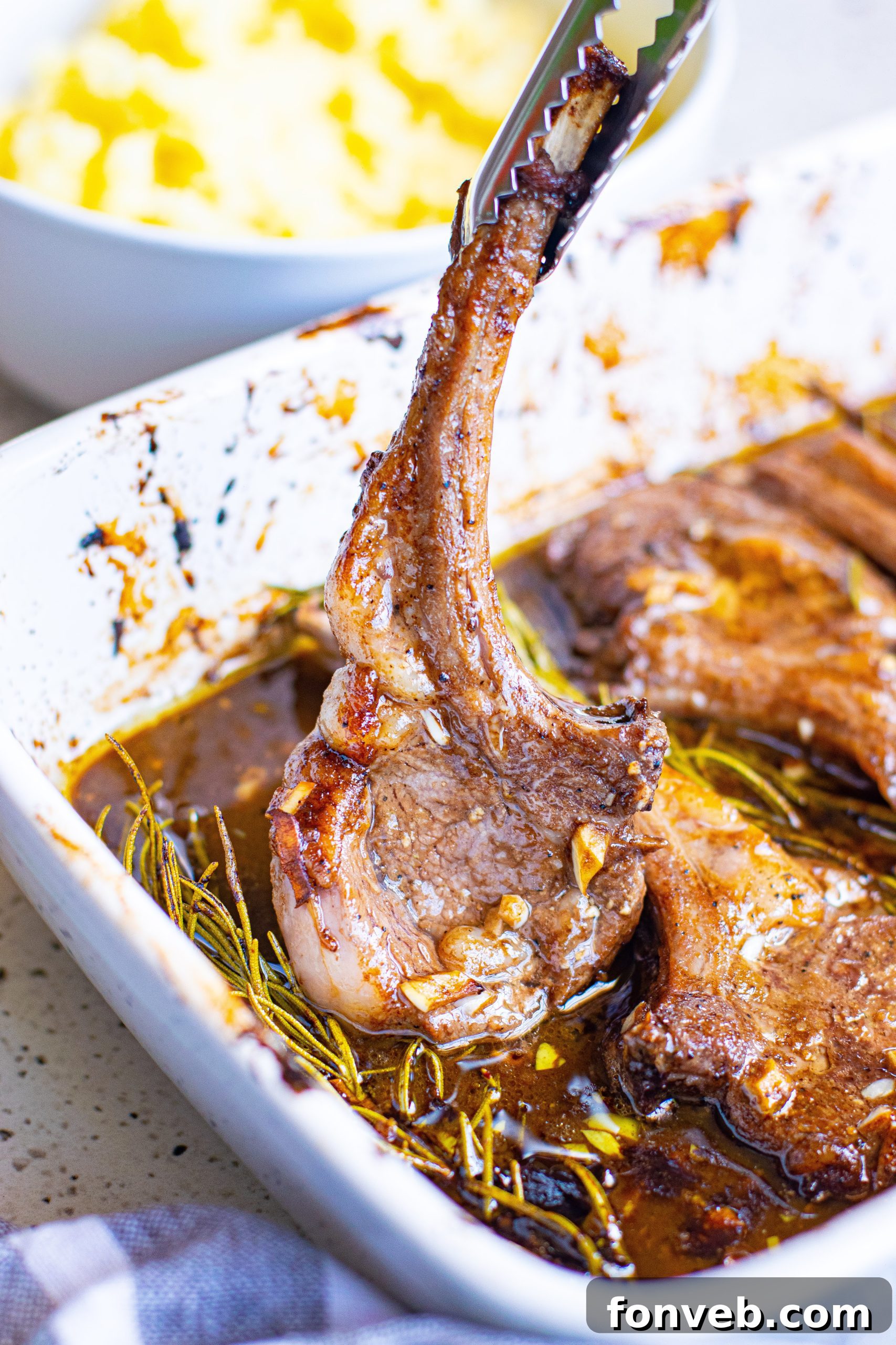 Close-up of a plate with a lamb chop drizzled with a rich sauce, alongside a sprig of rosemary
