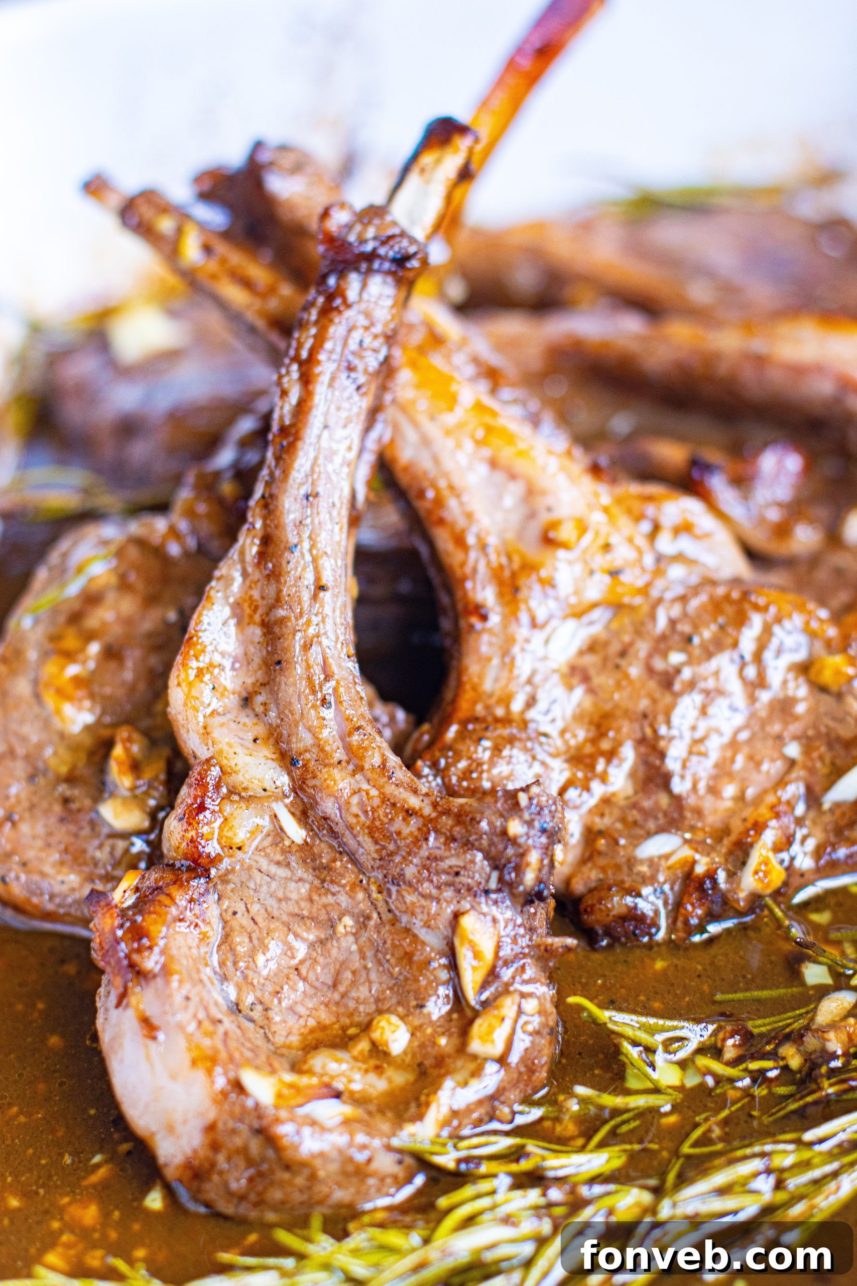 A large skillet on a stovetop, with several lamb chops being seared to a golden-brown perfection