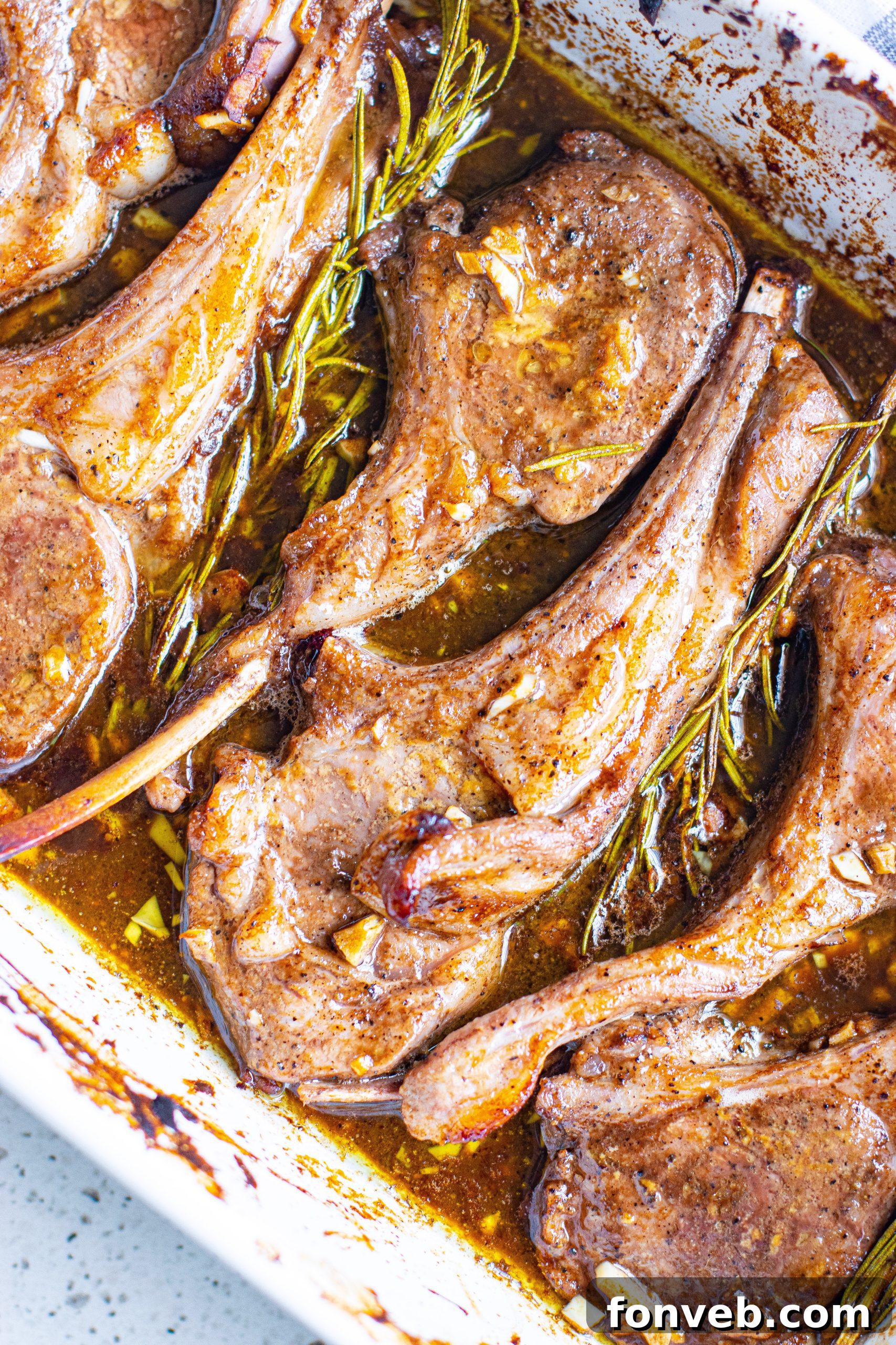 Two plates of cooked balsamic garlic lamb chops, each served with a sprig of fresh rosemary