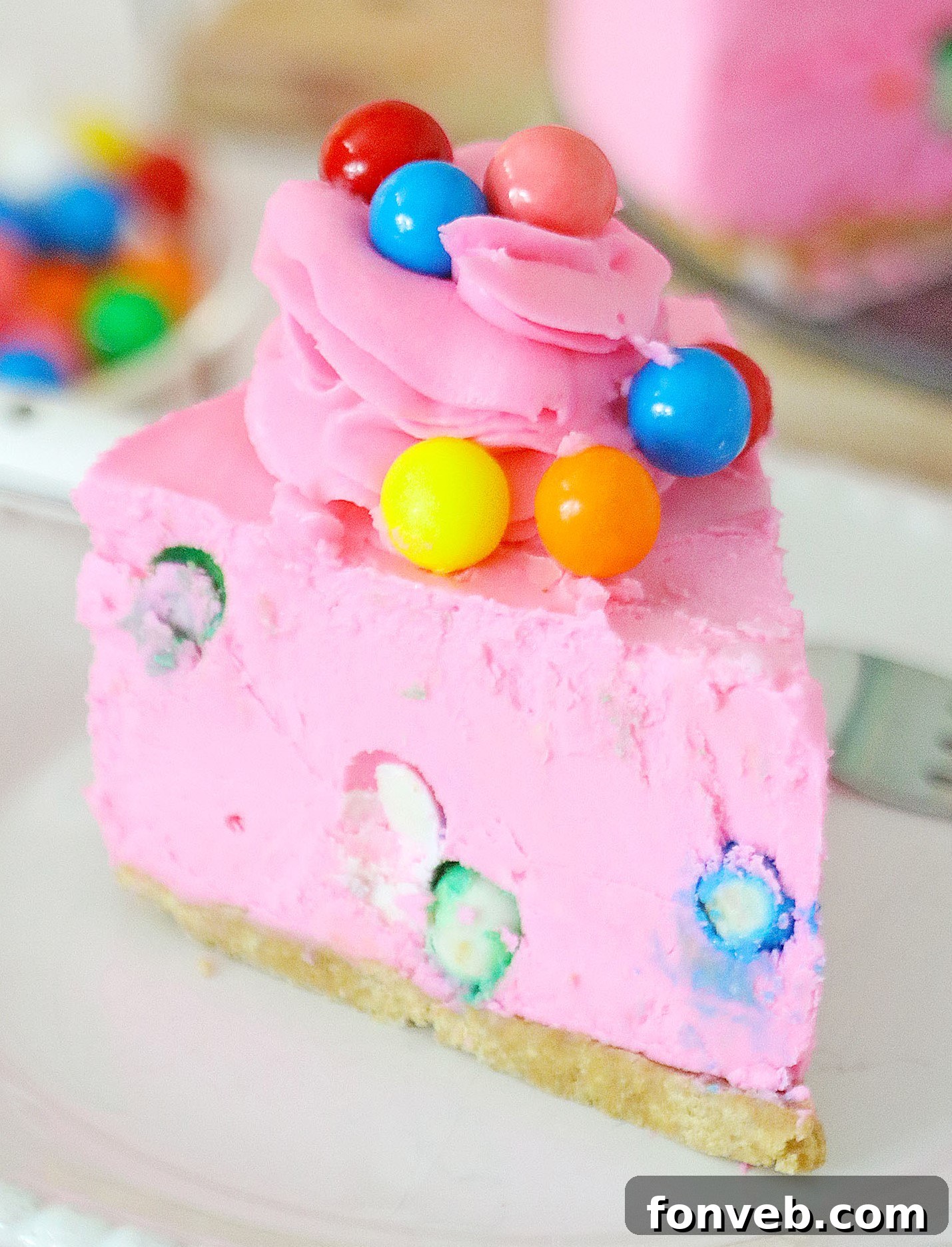 A beautifully sliced piece of pink bubblegum cheesecake, showcasing the gumballs embedded within the creamy filling and the perfect graham cracker crust.