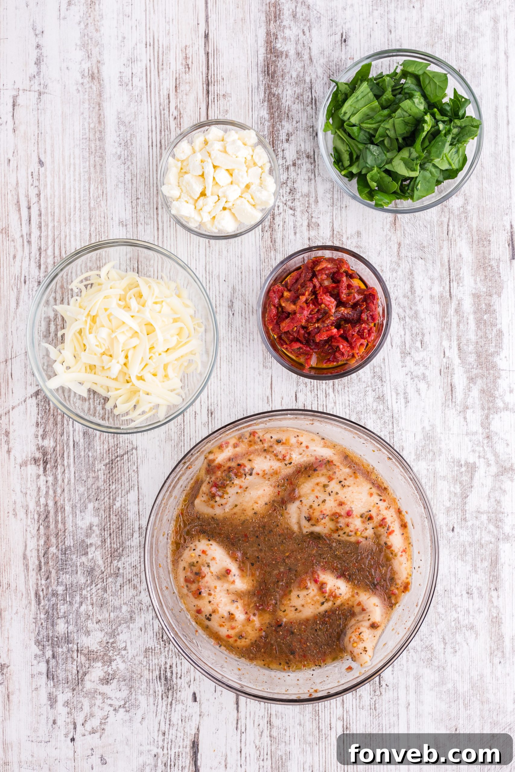 A selection of fresh ingredients including sundried tomatoes, spinach, cheeses, and chicken breasts