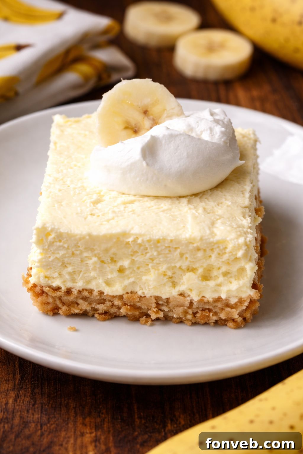 A single Banana Cream Cheesecake Bar elegantly presented on a white plate, showcasing its golden crust, creamy filling, and fresh banana slices on top.