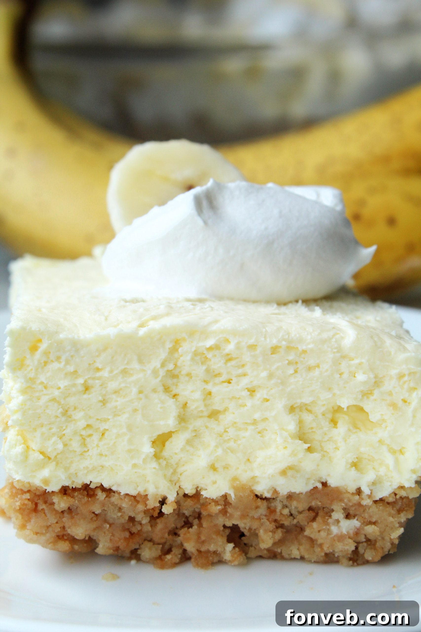 Close-up of a tray of freshly made Banana Cream Cheesecake Bars, garnished with whipped cream and banana slices, ready to be served.