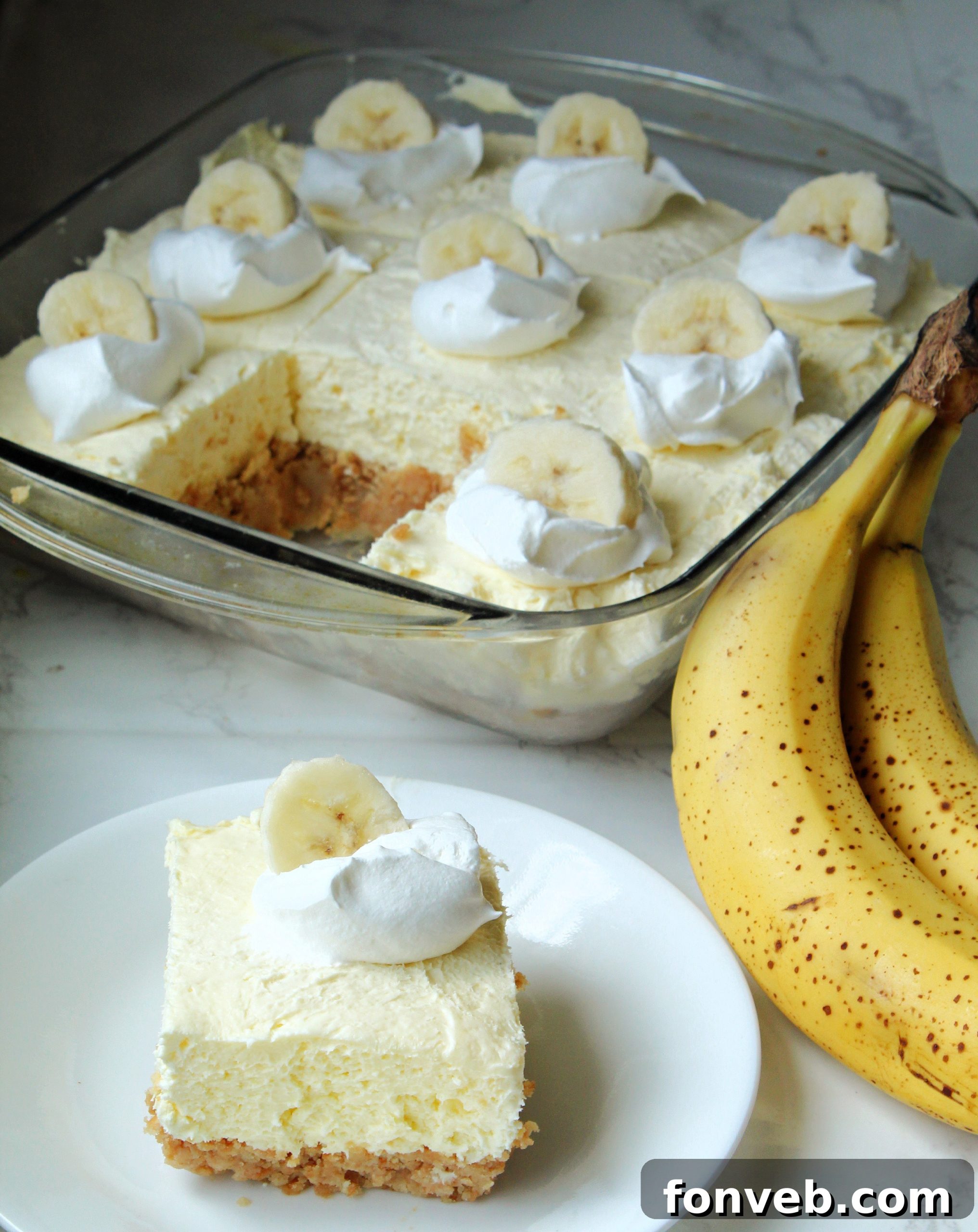 A close-up of a sliced Banana Cream Cheesecake Bar, showing the distinct layers of crust, creamy filling, and a fresh banana slice. 