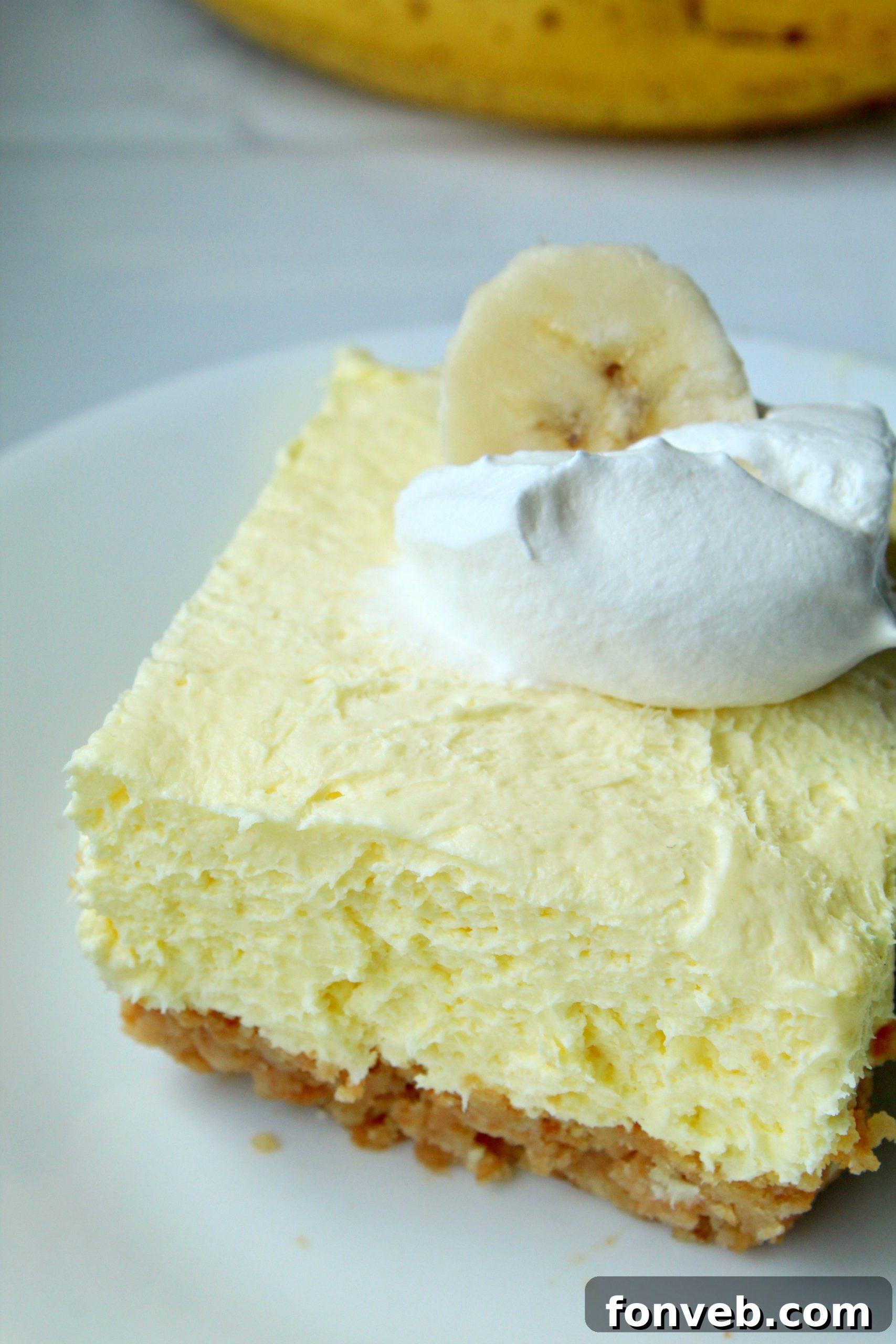 A generous slice of Banana Cream Cheesecake Bar with a golden crust, rich filling, and a fresh banana slice on top, ready for serving.