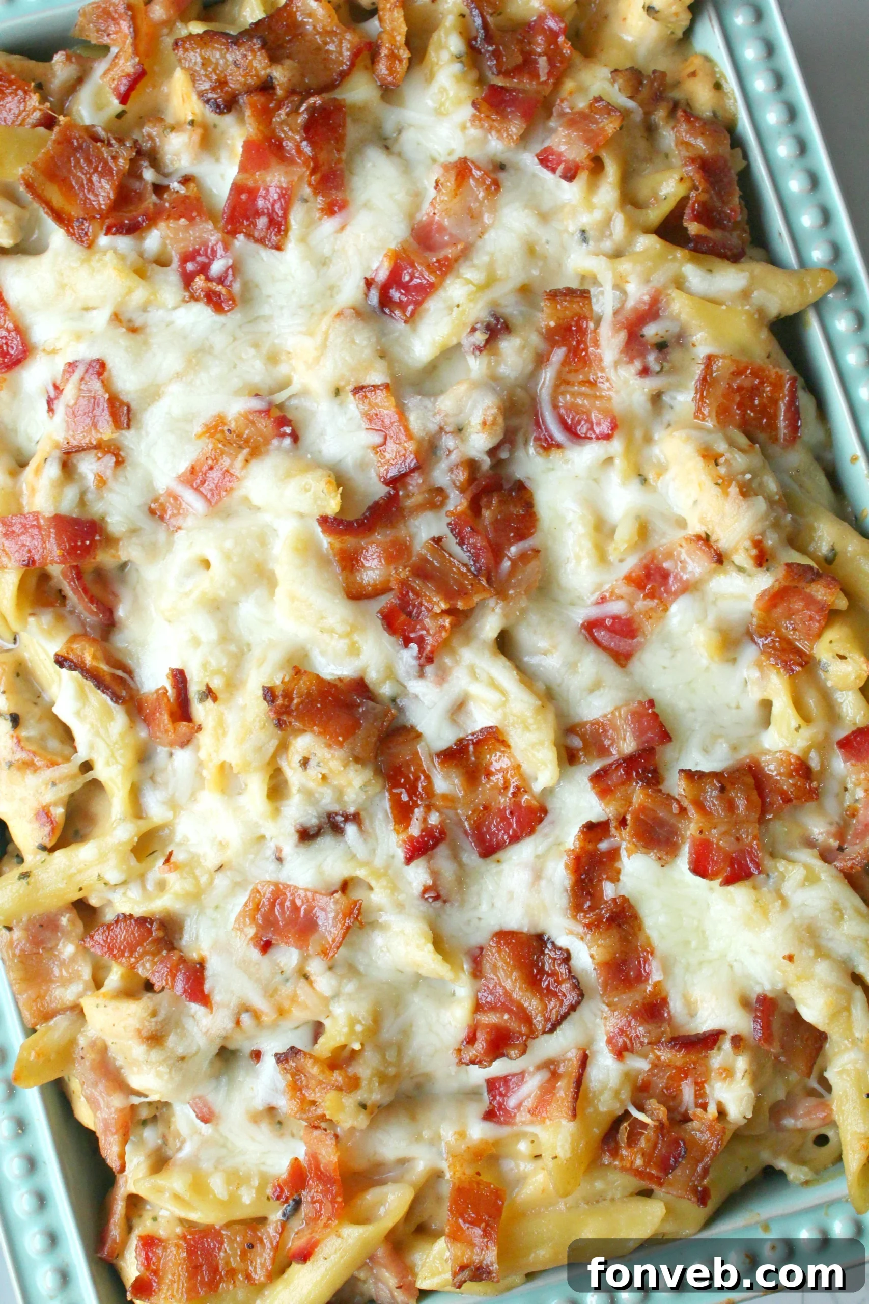 A serving spoon lifting a portion of the Chicken Bacon Ranch Penne, showcasing its creamy sauce and a strand of melted cheese.