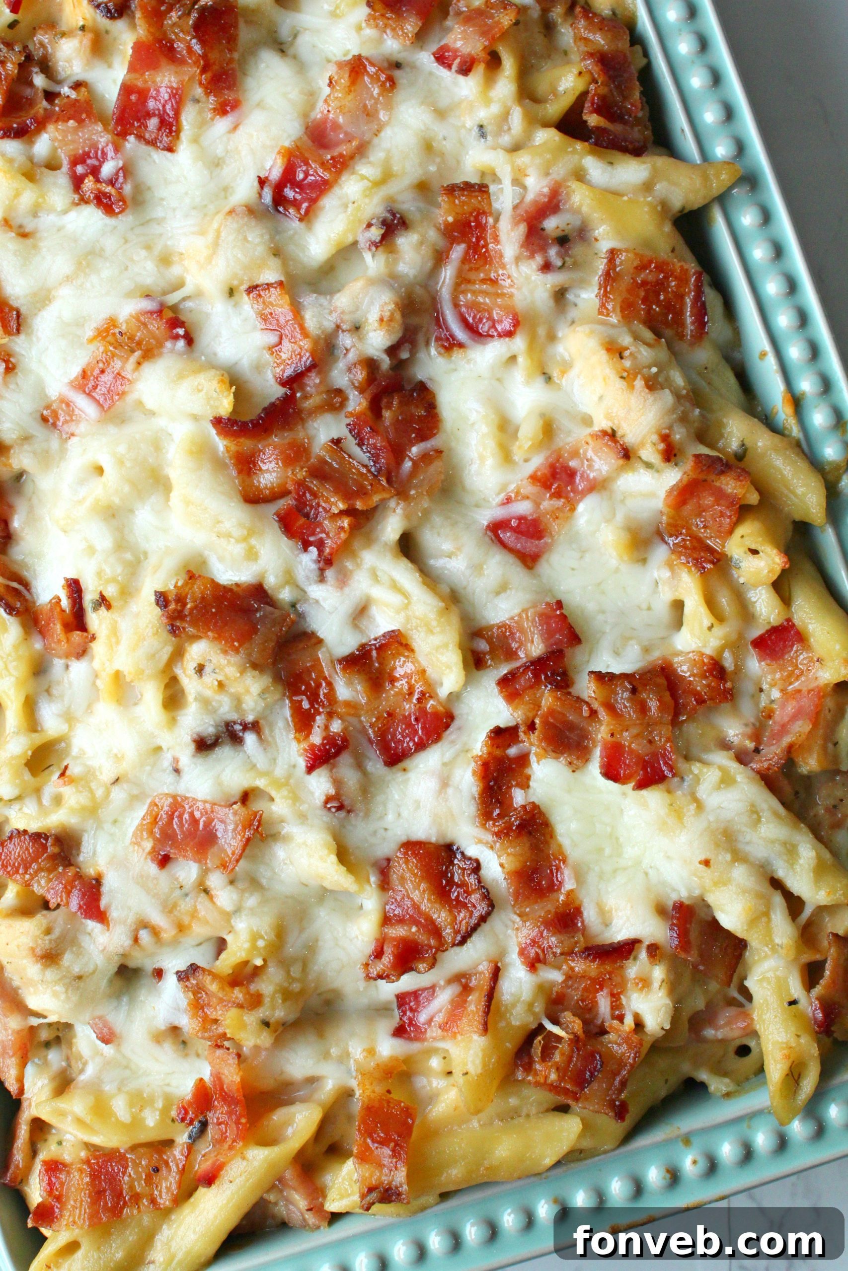 Chopped chicken breast cubes, seasoned and ready for cooking, in a bowl beside the uncooked penne pasta.