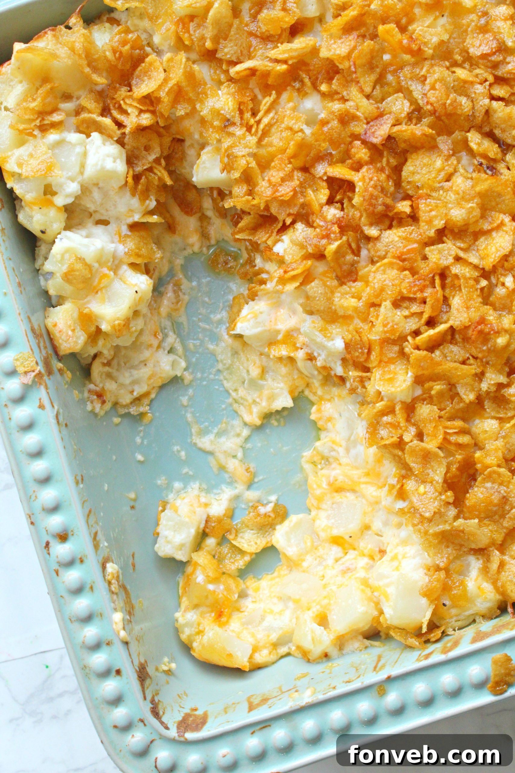 A baking pan of Funeral Potatoes with a few servings already taken, showing the gooey cheese inside