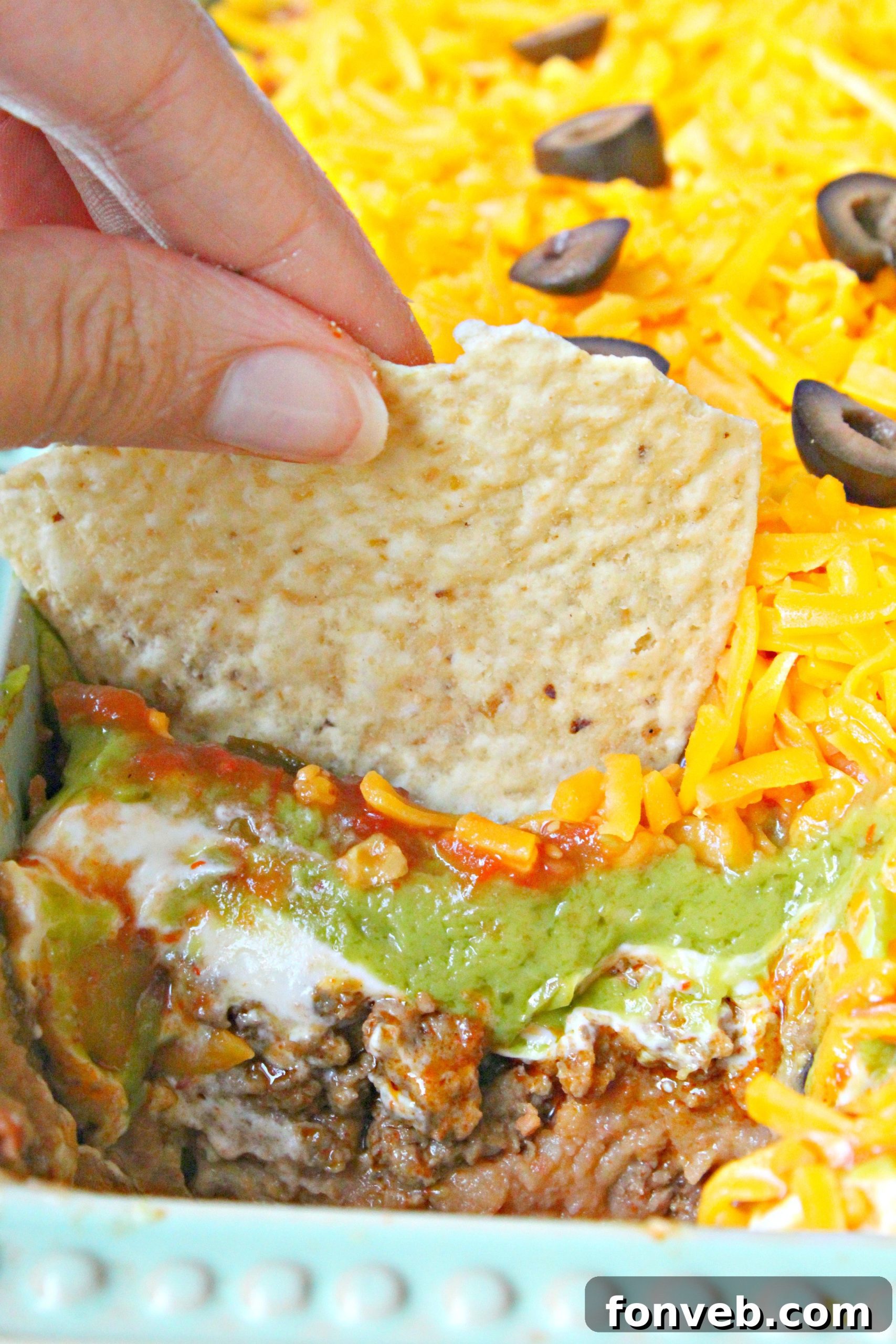 7 Layer Taco Dip 4 7 layer taco dip with a tortilla chip being dipped in