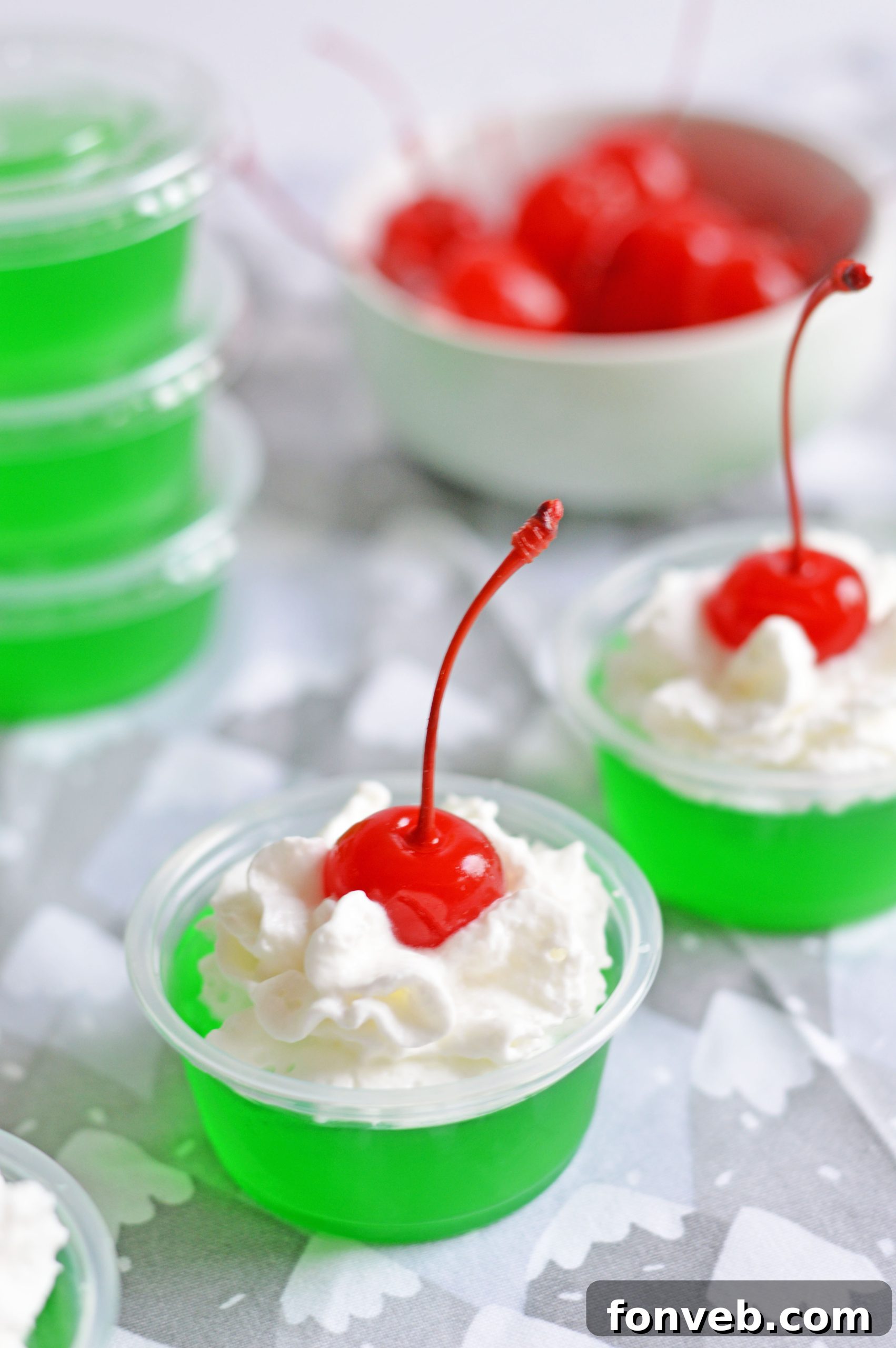 Bright green Grinch Jello Shots in small cups with whipped cream and a cherry on top