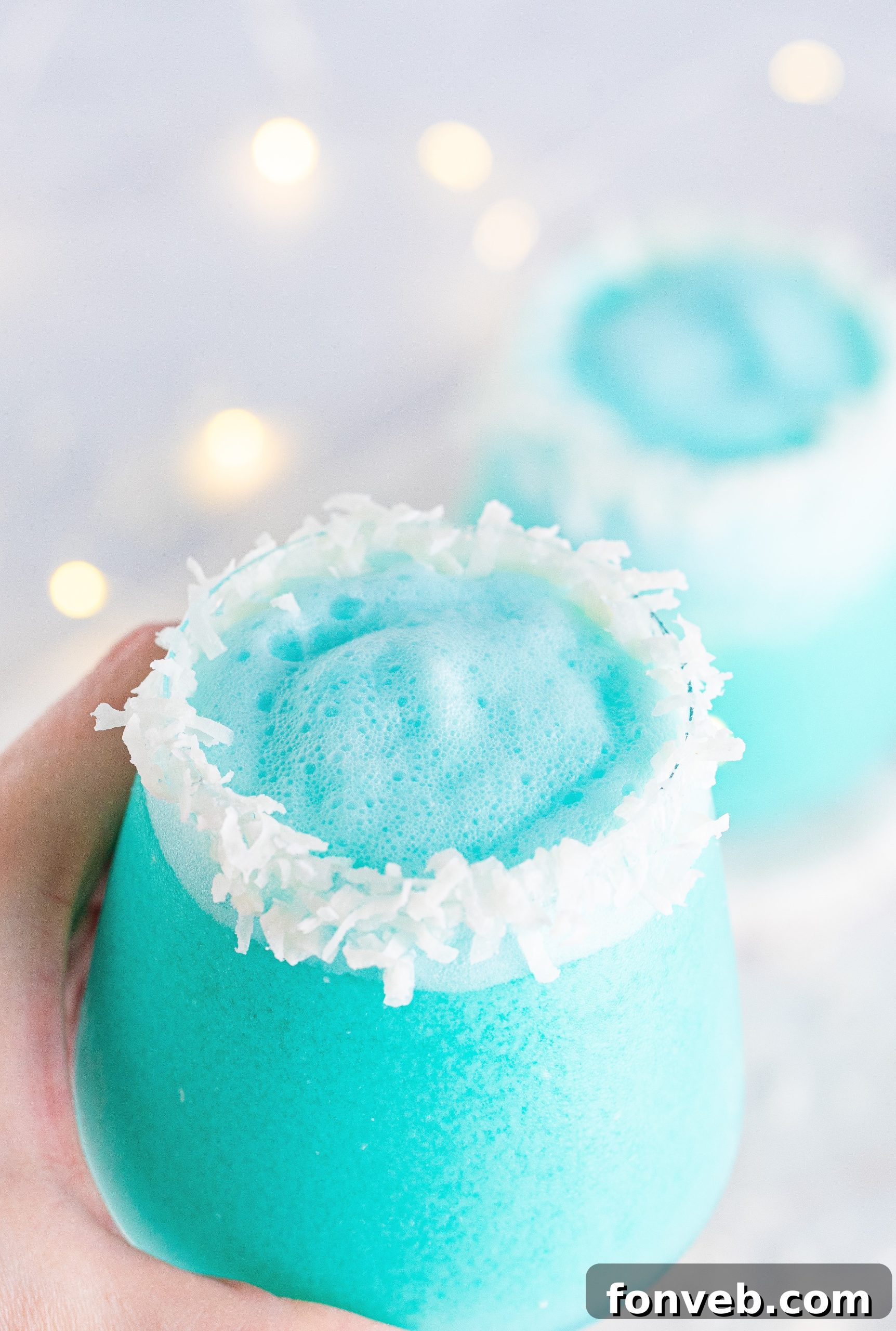 Jack Frost Cocktail served in a glass with a coconut rim, sparkling and icy blue, ready for a festive celebration.