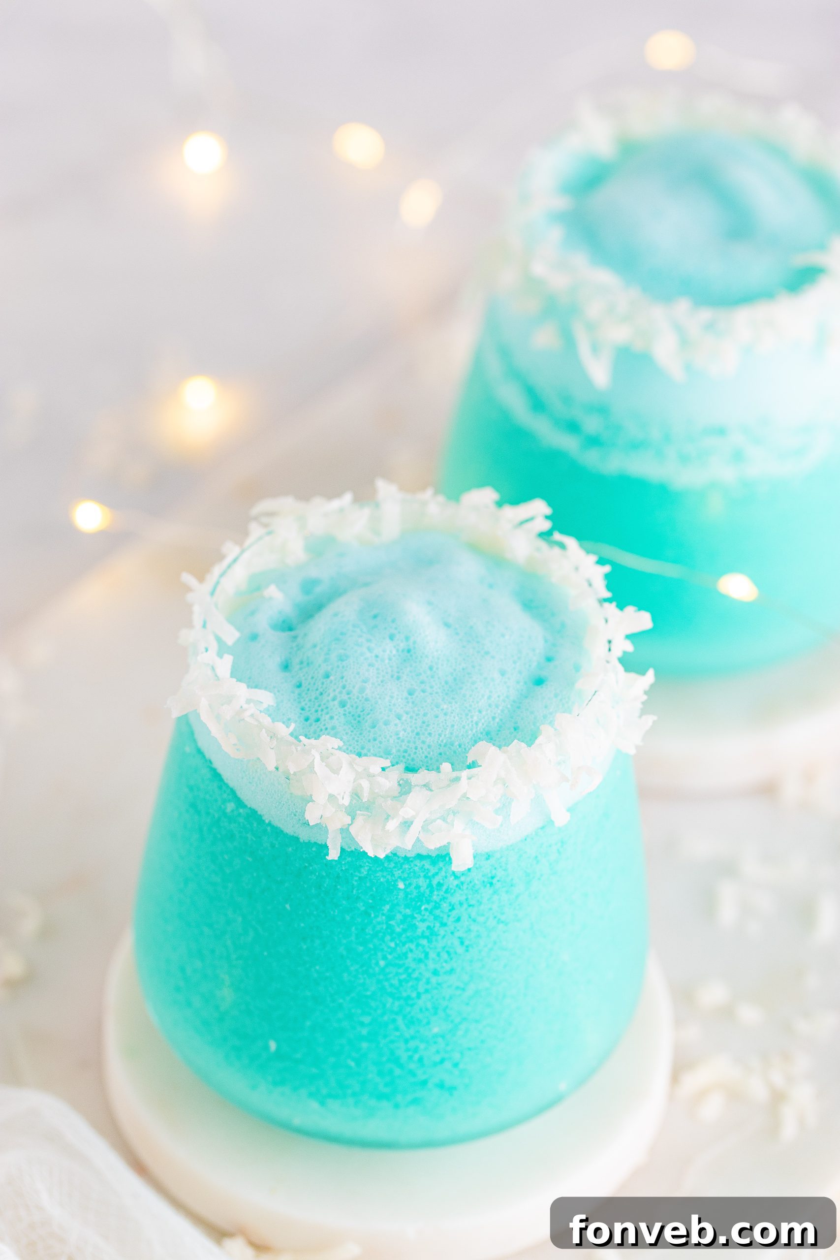 A close-up of a Jack Frost Cocktail in a glass, featuring the blue drink and coconut flakes on the rim against a festive background.