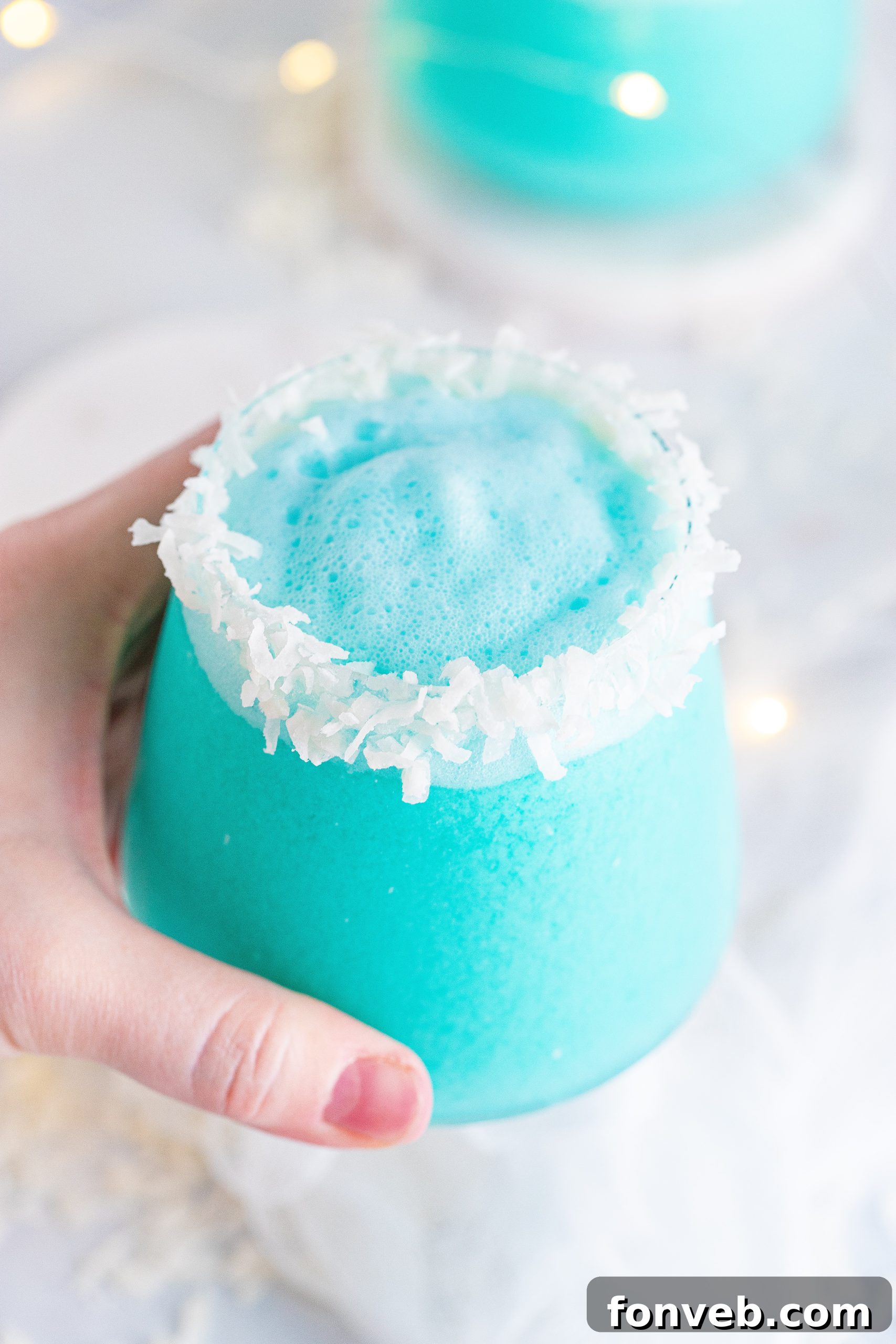 Two glasses of Jack Frost Cocktail, one with a prominent coconut rim, positioned on a white surface with holiday decorations.