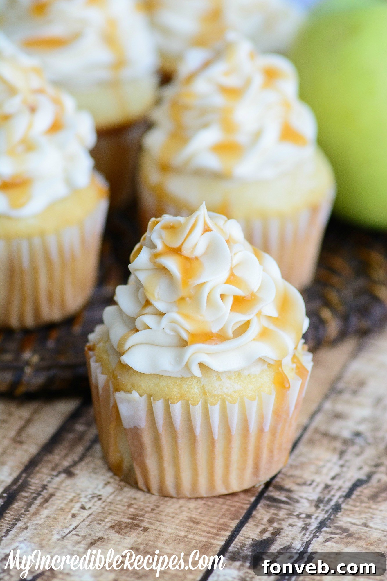 Overhead shot of two beautifully frosted caramel apple cupcakes on a light background.