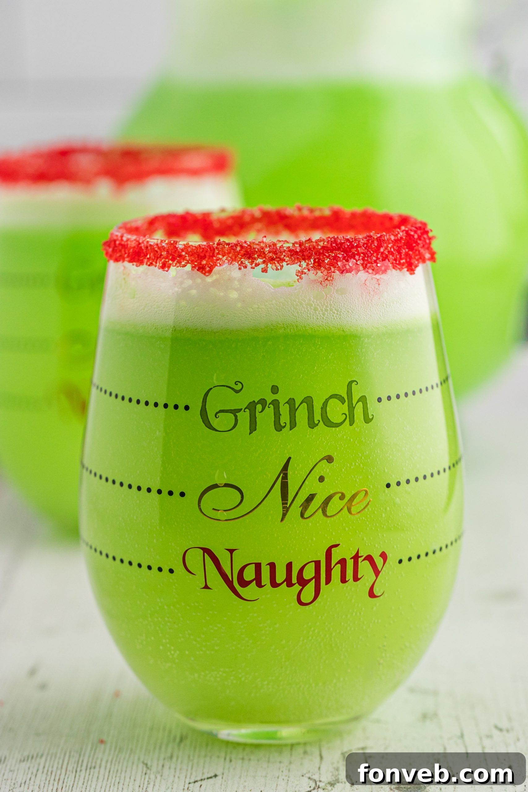 A large punch bowl filled with Grinch Punch, with scoops of melting sherbet and festive garnishes.