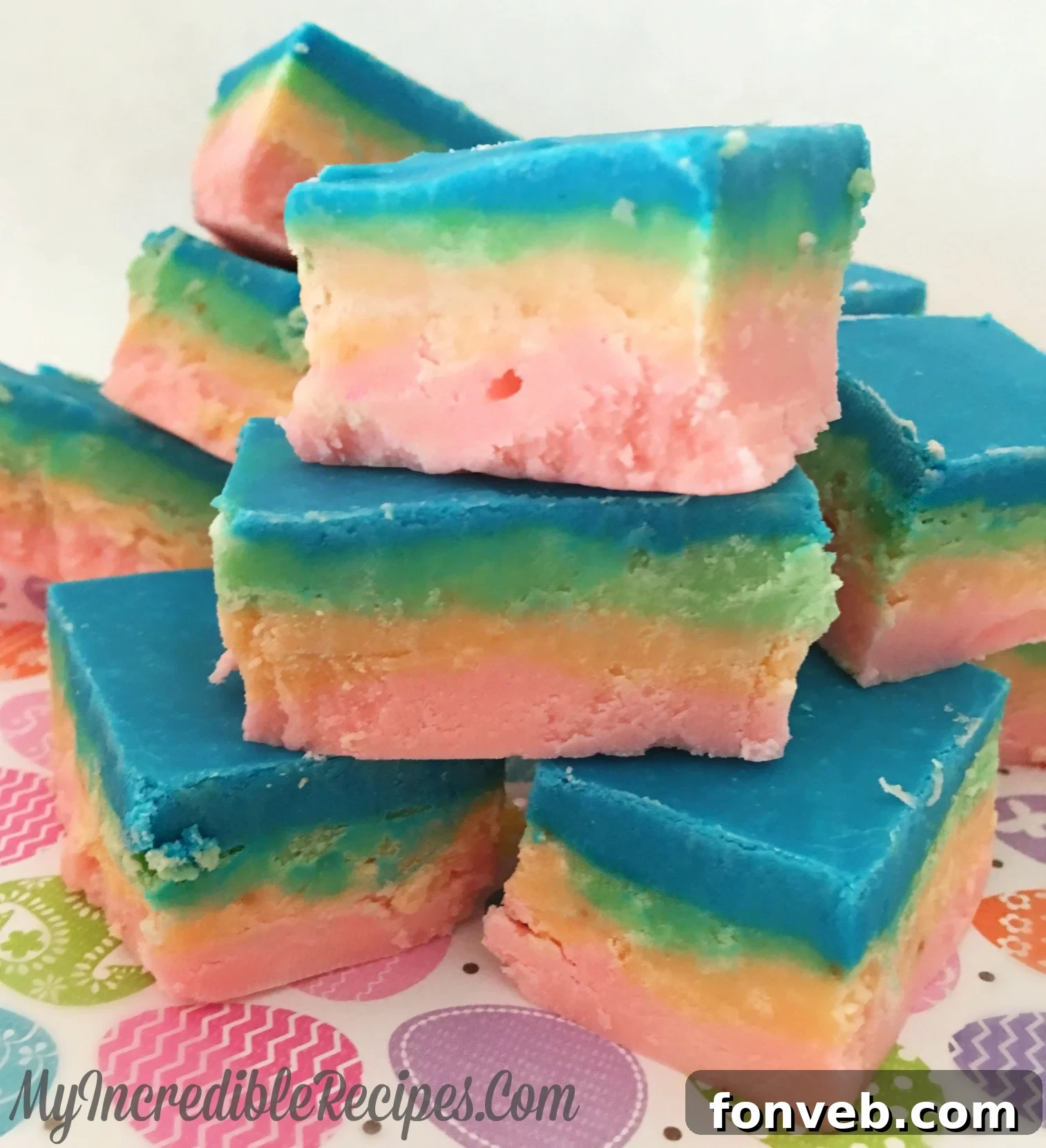 Close-up of vibrant, colorful Unicorn Fudge squares arranged artfully, showcasing pink, orange, green, and blue layers, ready to be enjoyed.